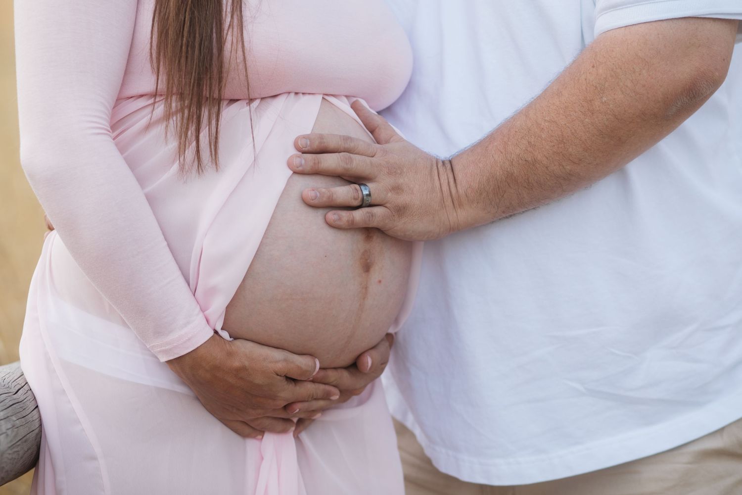 Close up maternity photo of expecting parents holding mom’s baby bump.