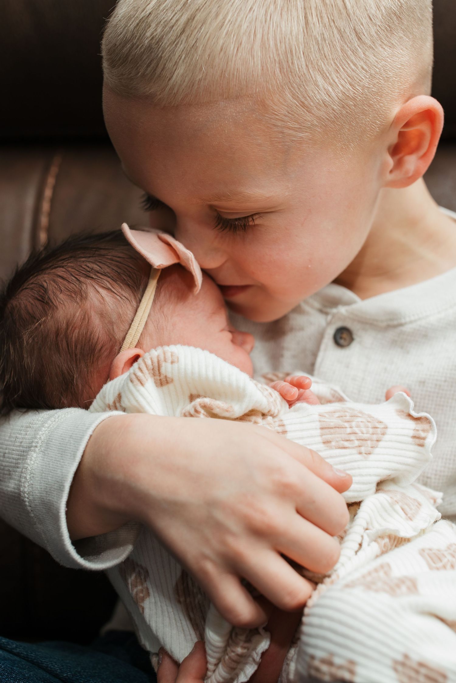 Big brother snuggling and kissing his newborn sister during their cozy in-home session in Middleton, Idaho.