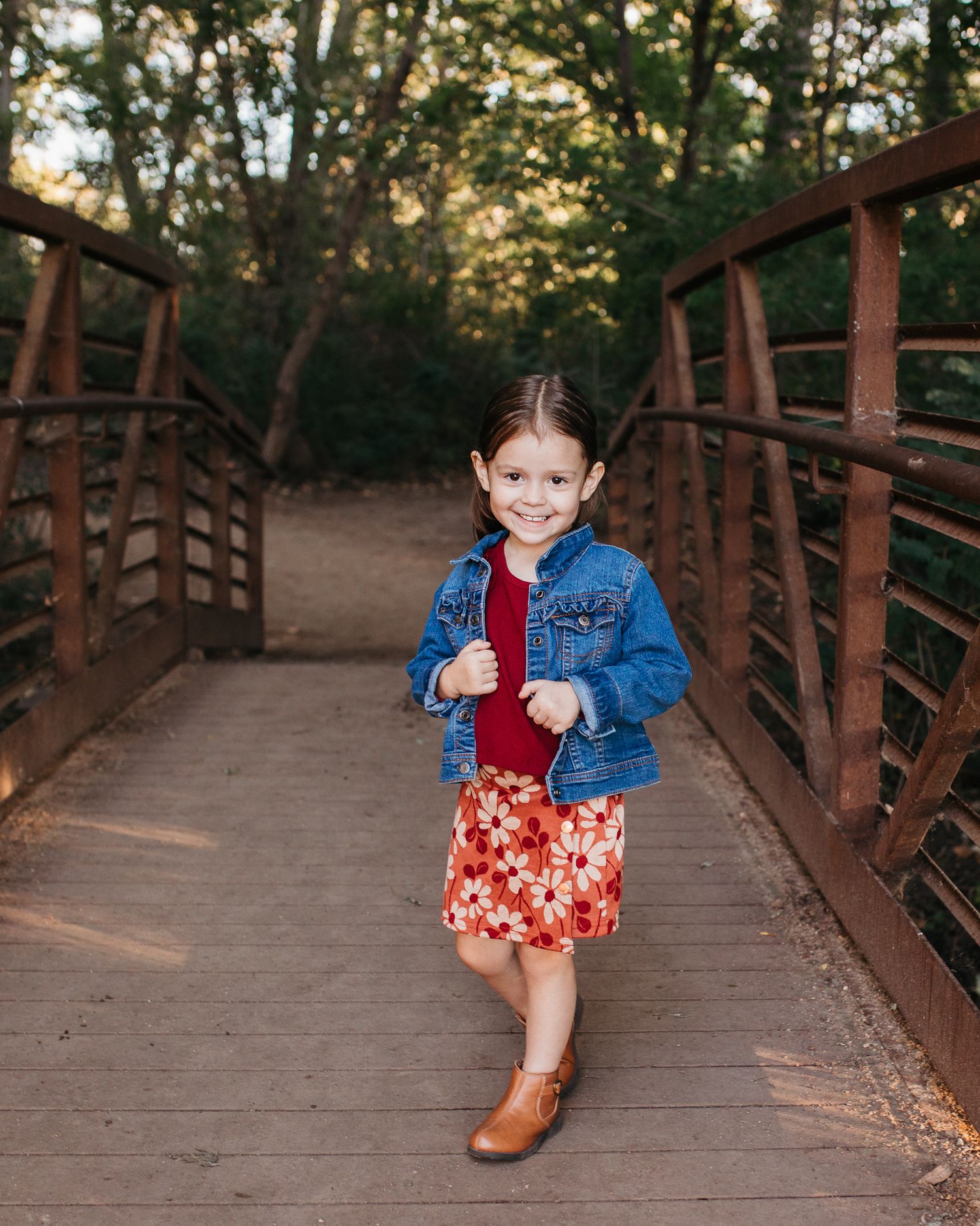 A child wearing a denim jacket and floral dress poses playfully on a wooden bridge walkway at sunset - annual birthday milestone Nampa