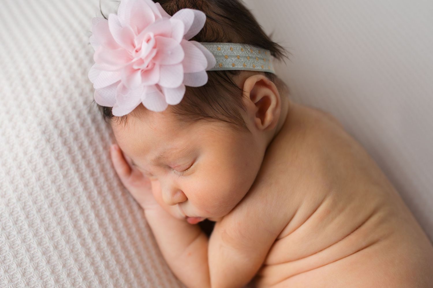 Studio newborn photography portrait of a sleeping baby girl wearing a pink flower headband, posed on a soft neutral blanket in Caldwell, ID