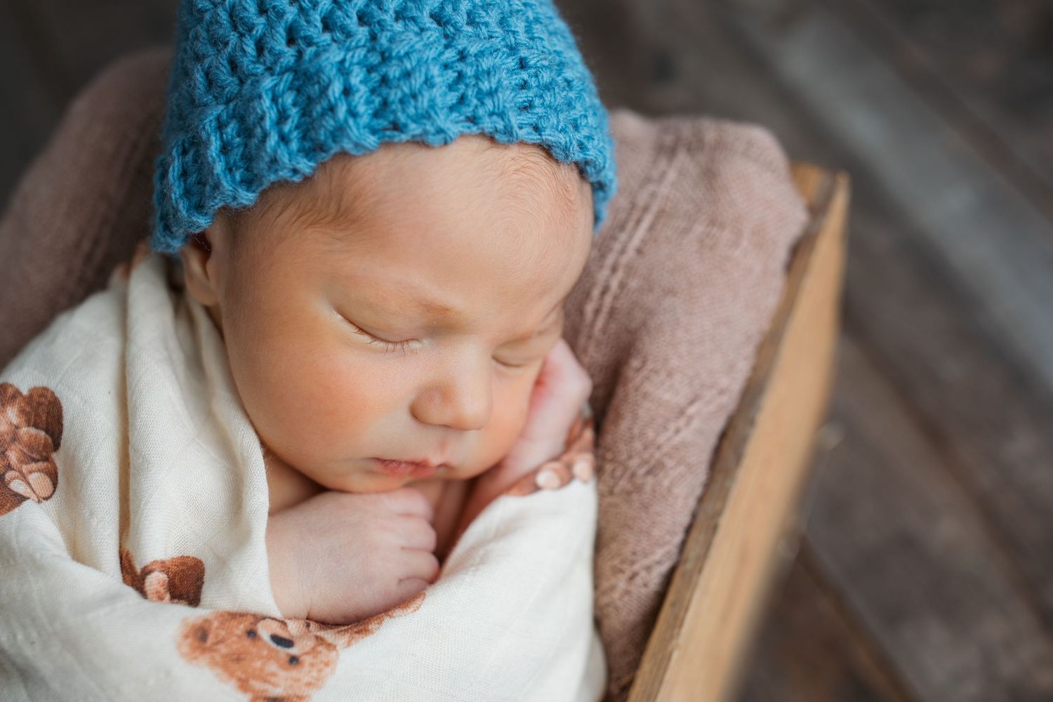 Close-up of newborn baby boy sleeping in blue knit hat wrapped in teddy bear blanket during studio newborn session
