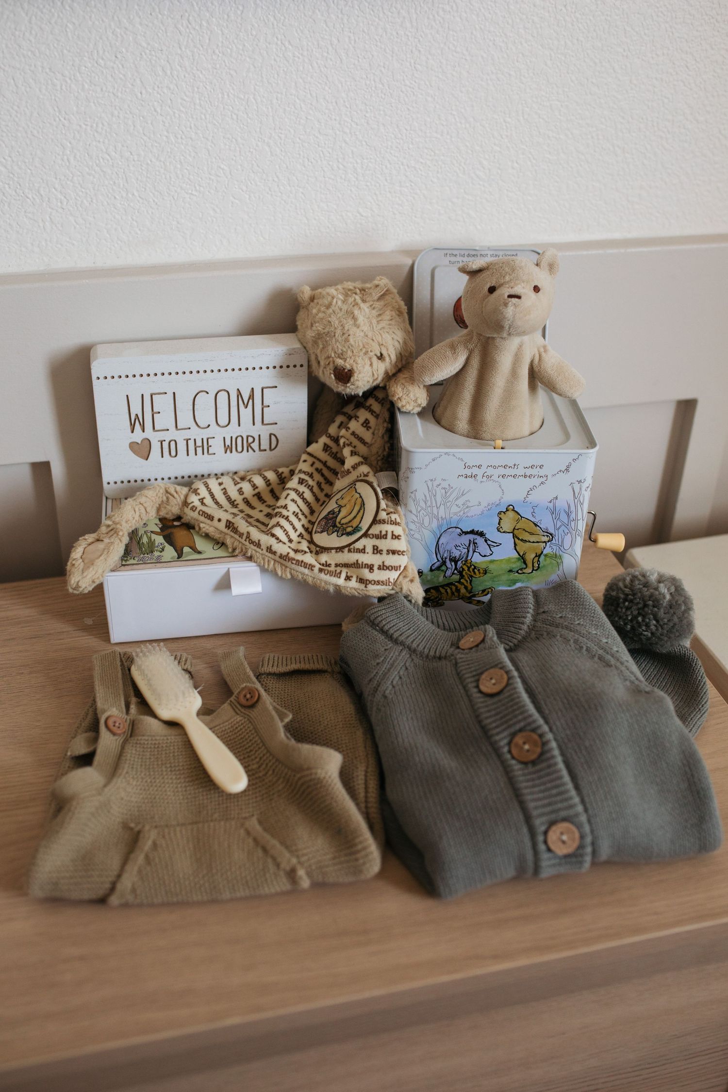 Baby nursery items including knit clothing, stuffed animals, and a 'Welcome to the World' sign arranged on wooden surface - lifestyle photos