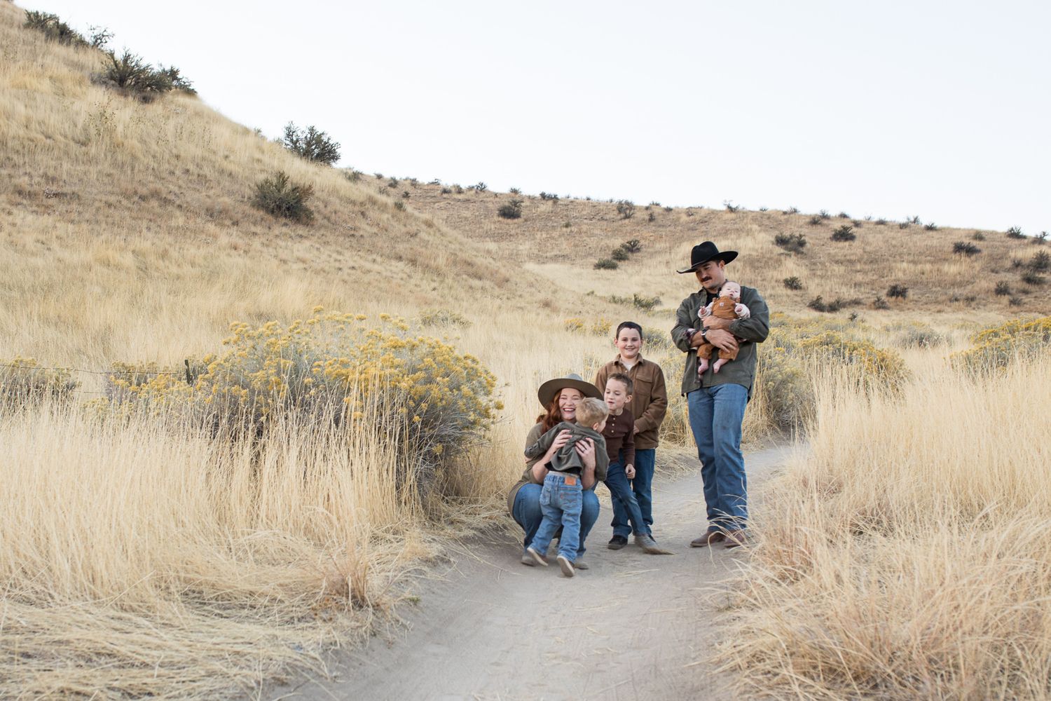 A family walks along a winding dirt trail through dry golden grass on a hillside during autumn - lifestyle family photos in Boise