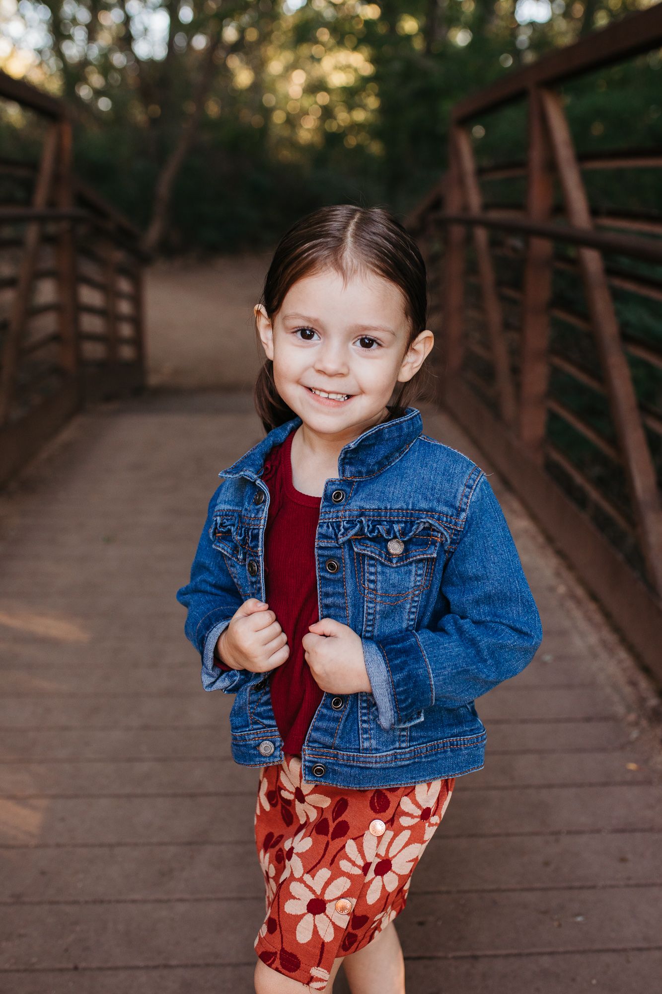A child wearing a denim jacket and red floral dress poses on a wooden bridge - birthday milestone photos Boise Idaho