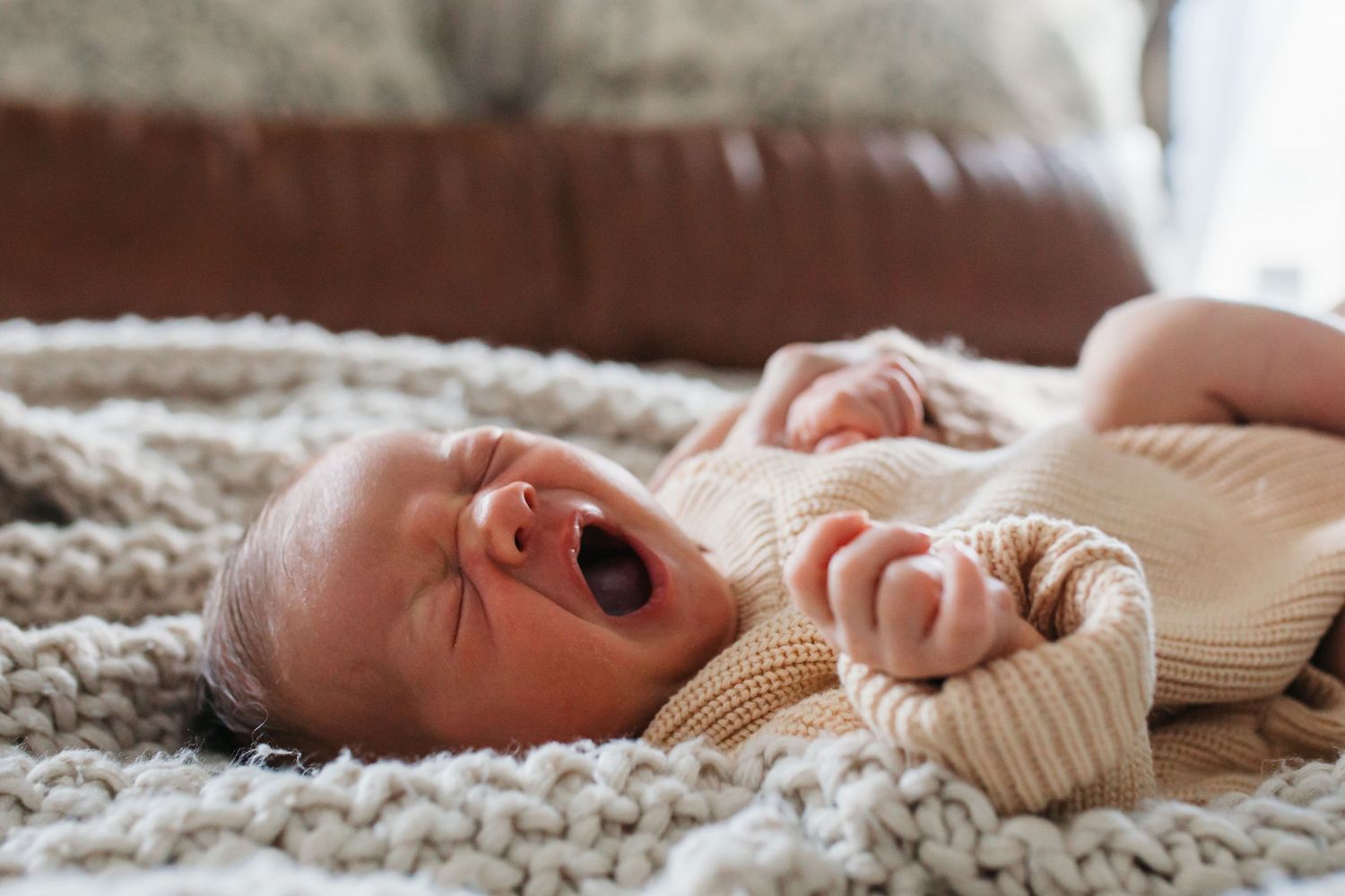A sleepy baby in a cream-colored knit sweater lies on a textured beige blanket - lifestyle in-home newborn photos Boise