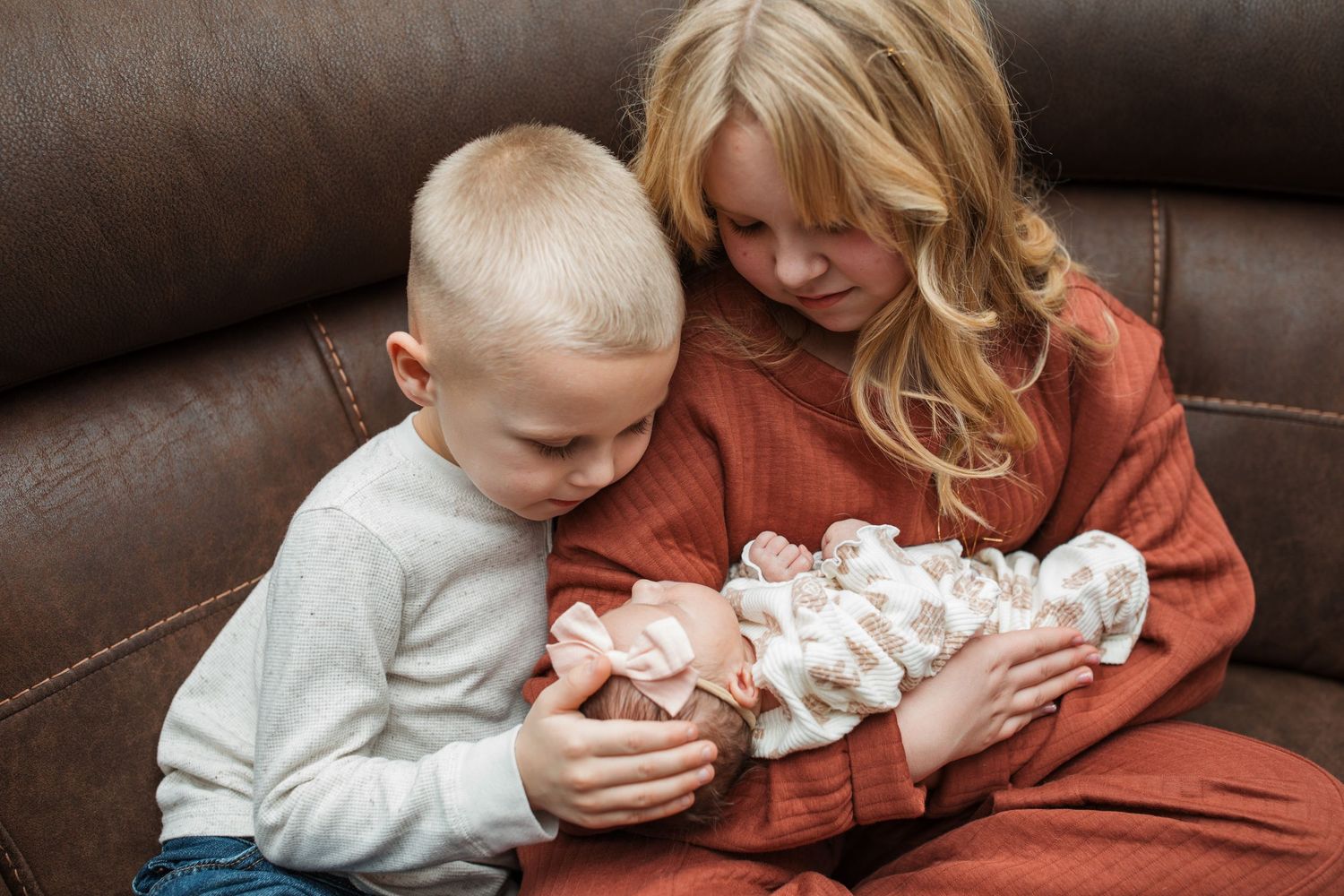 Big brother and sister gently holding their newborn sibling during an in-home session in Middleton, Idaho.