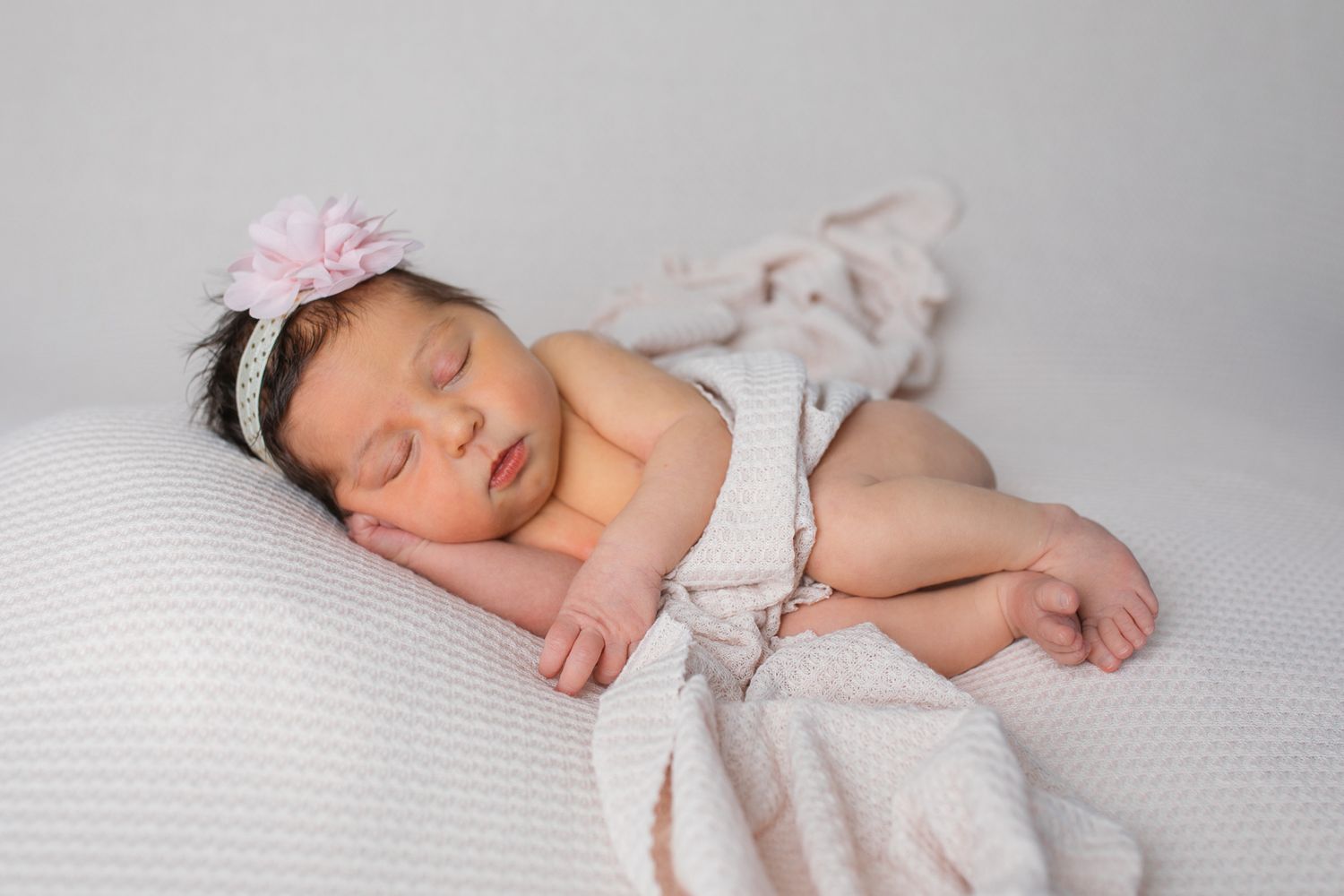A sleeping newborn baby lies peacefully on soft white textured fabric in a minimalist studio setting  studio newborn photography Caldwell ID
