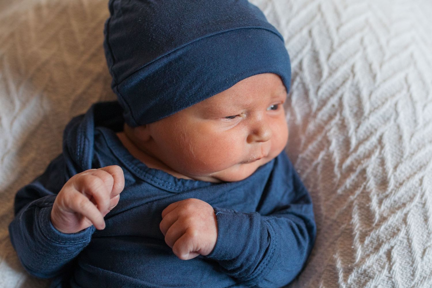 newborn baby in navy blue clothing lying on white bedding. Fresh 48 session by Sara Elizabeth Photography Boise Idaho