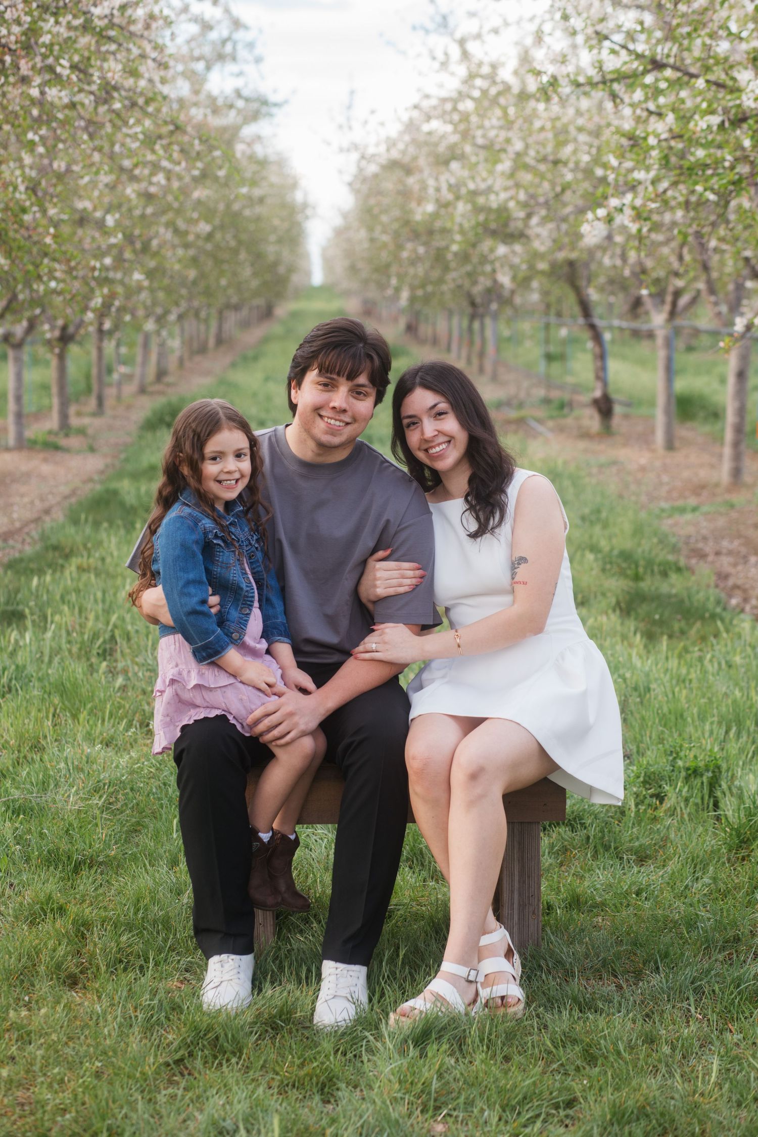 Family sitting together on bench in cherry blossom orchard at Cherry Hill Farms in Caldwell Idaho