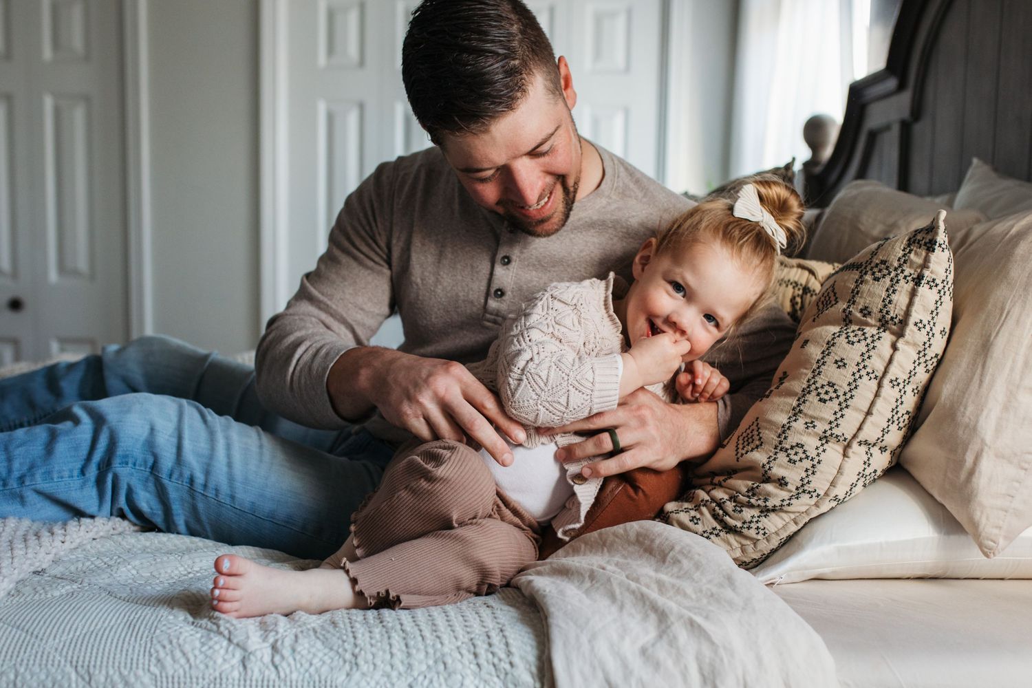A tender moment between parent and child playing together while relaxing on a bed with cozy pillows -in-home lifestyle family photos Boise