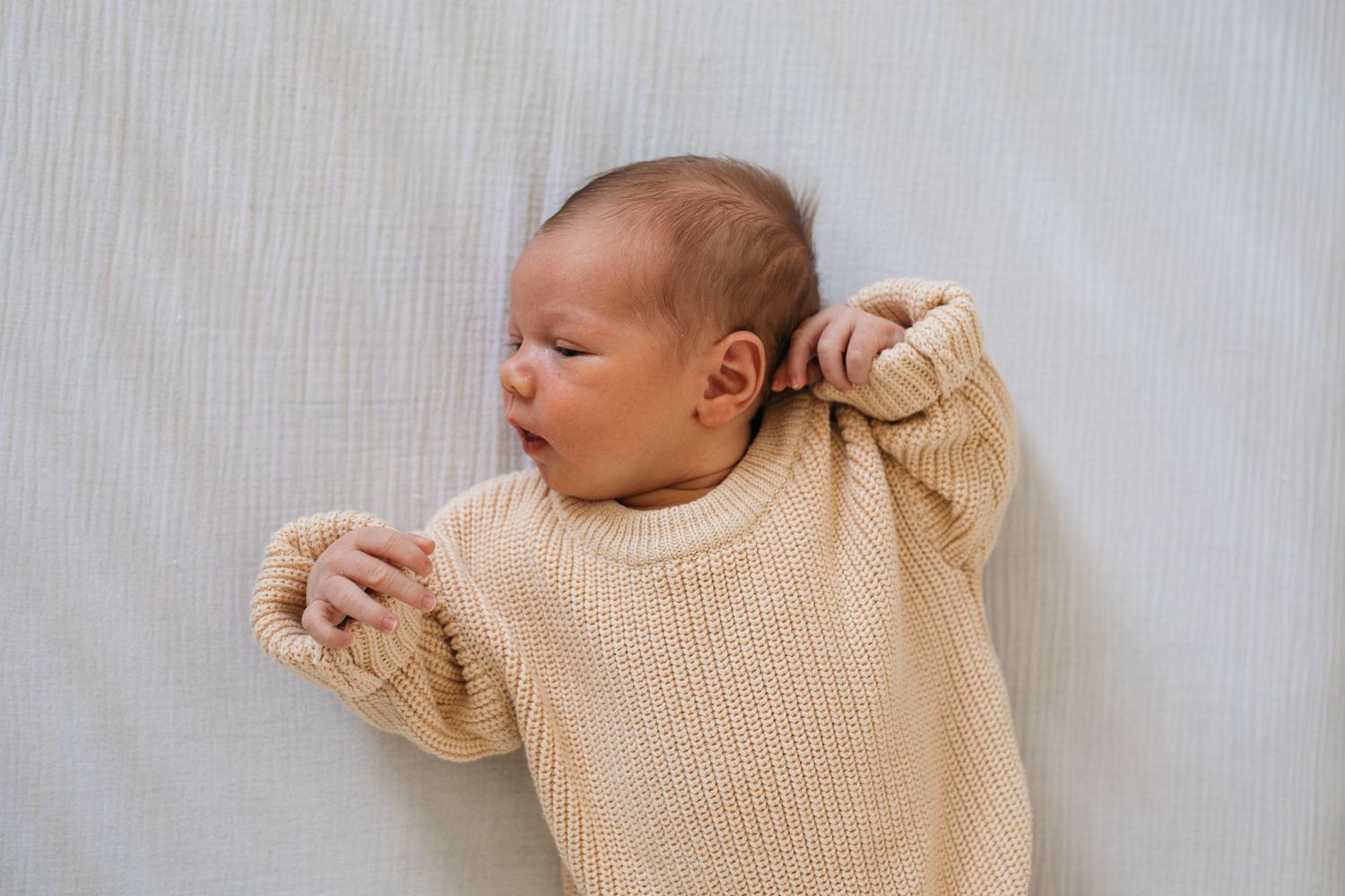 Newborn baby lying on a bed in a knitted onesie during an in-home lifestyle newborn session in Boise, Idaho.