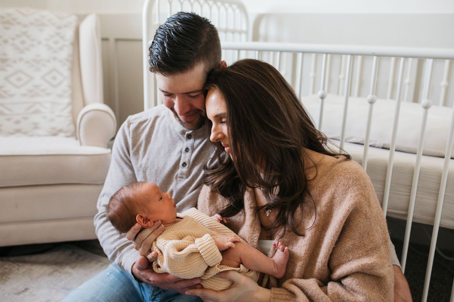 Parents holding their newborn during an in-home lifestyle session in a cozy neutral nursery in Boise, Idaho.