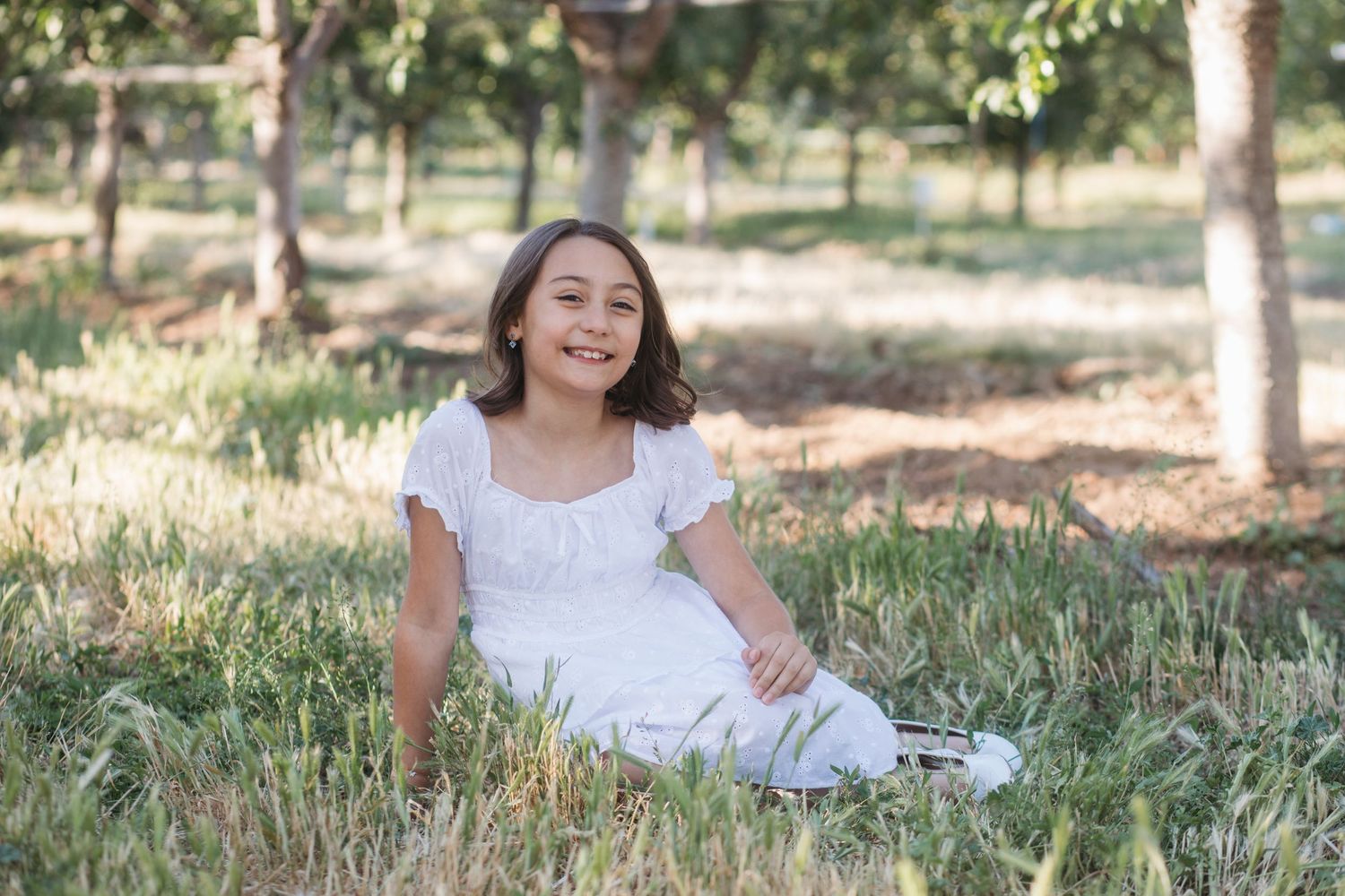 Young girl smiling in the grass during a relaxed orchard family session in Boise, Idaho.