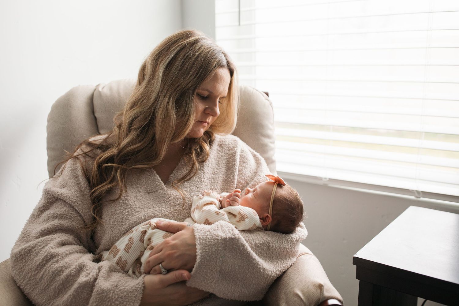 Mother holding her newborn in a cozy chair during a softly lit in-home lifestyle session in Middleton, Idaho.