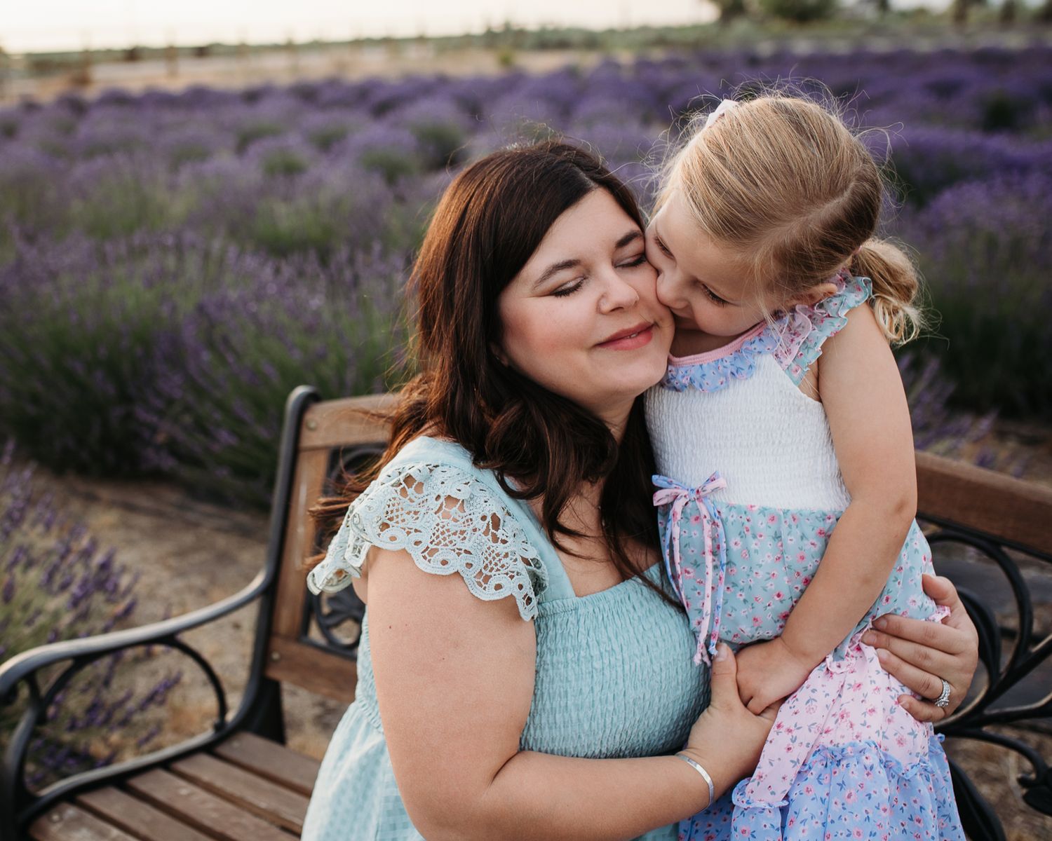 Two people in coordinating blue and white outfits share tender moments in a blooming lavender field at sunset - Maternity session in Boise,