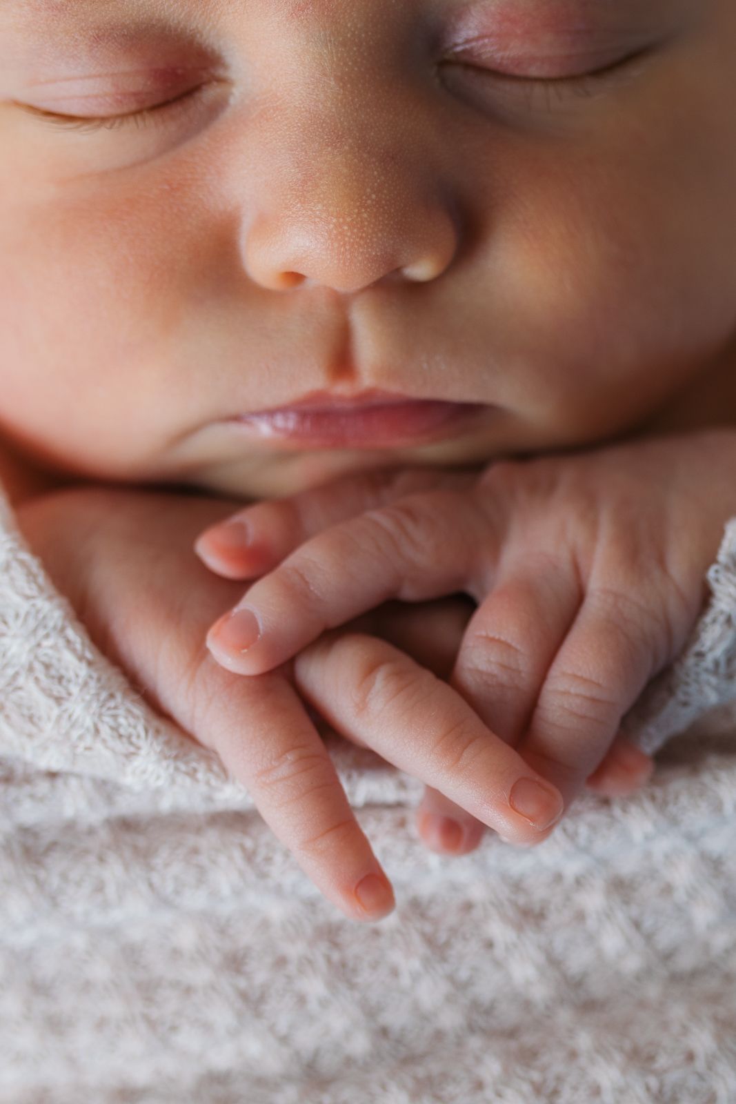 Close-up macro photography of a baby's delicate hands and mouth resting on soft white fabric.  studio newborn photography Caldwell Idaho