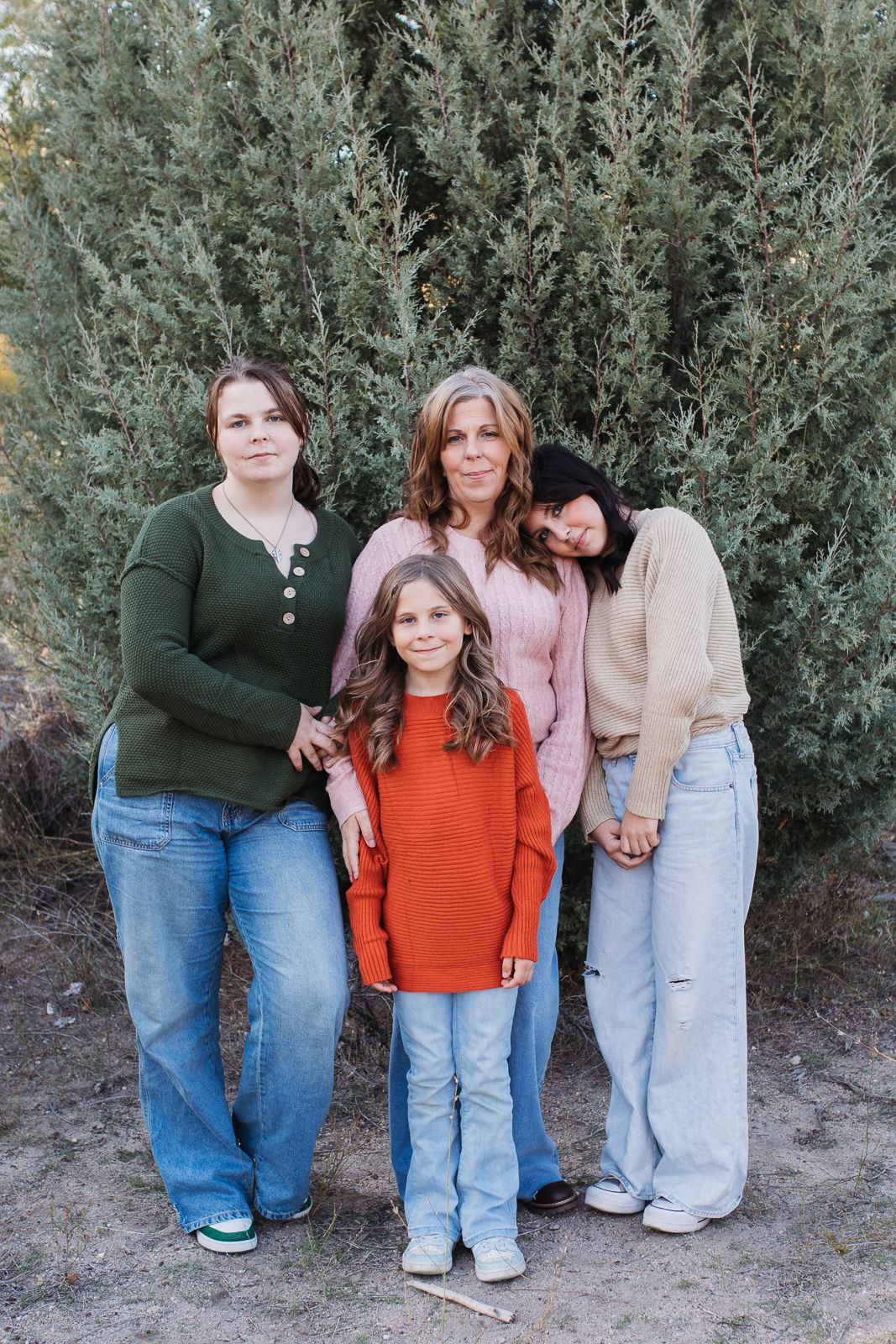 A group poses together against a backdrop of green foliage in casual denim and earth-toned clothing. Boise foothills family photography