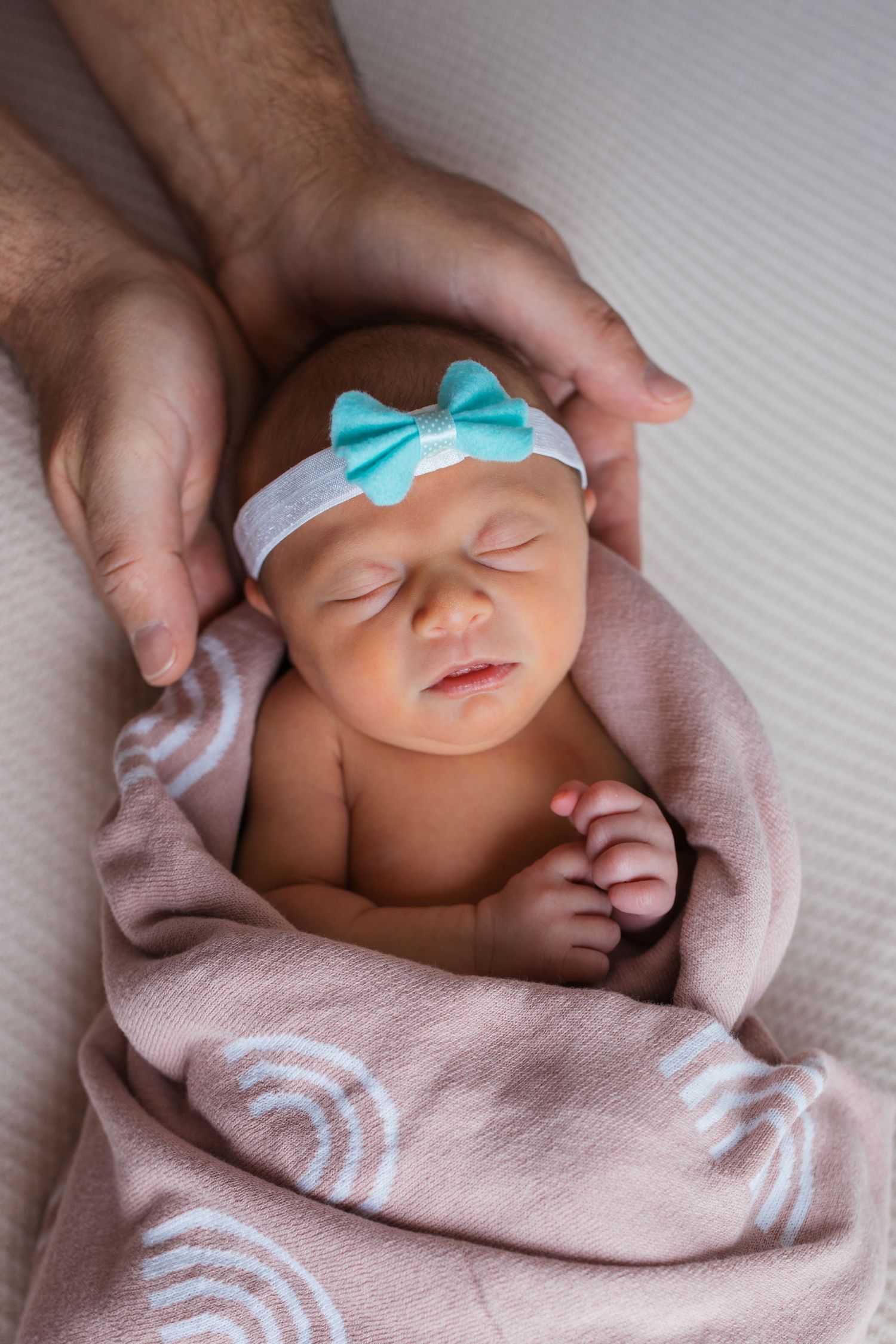 Newborn baby girl wrapped in pink with her parent’s hands gently framing her during a Nampa studio newborn session.