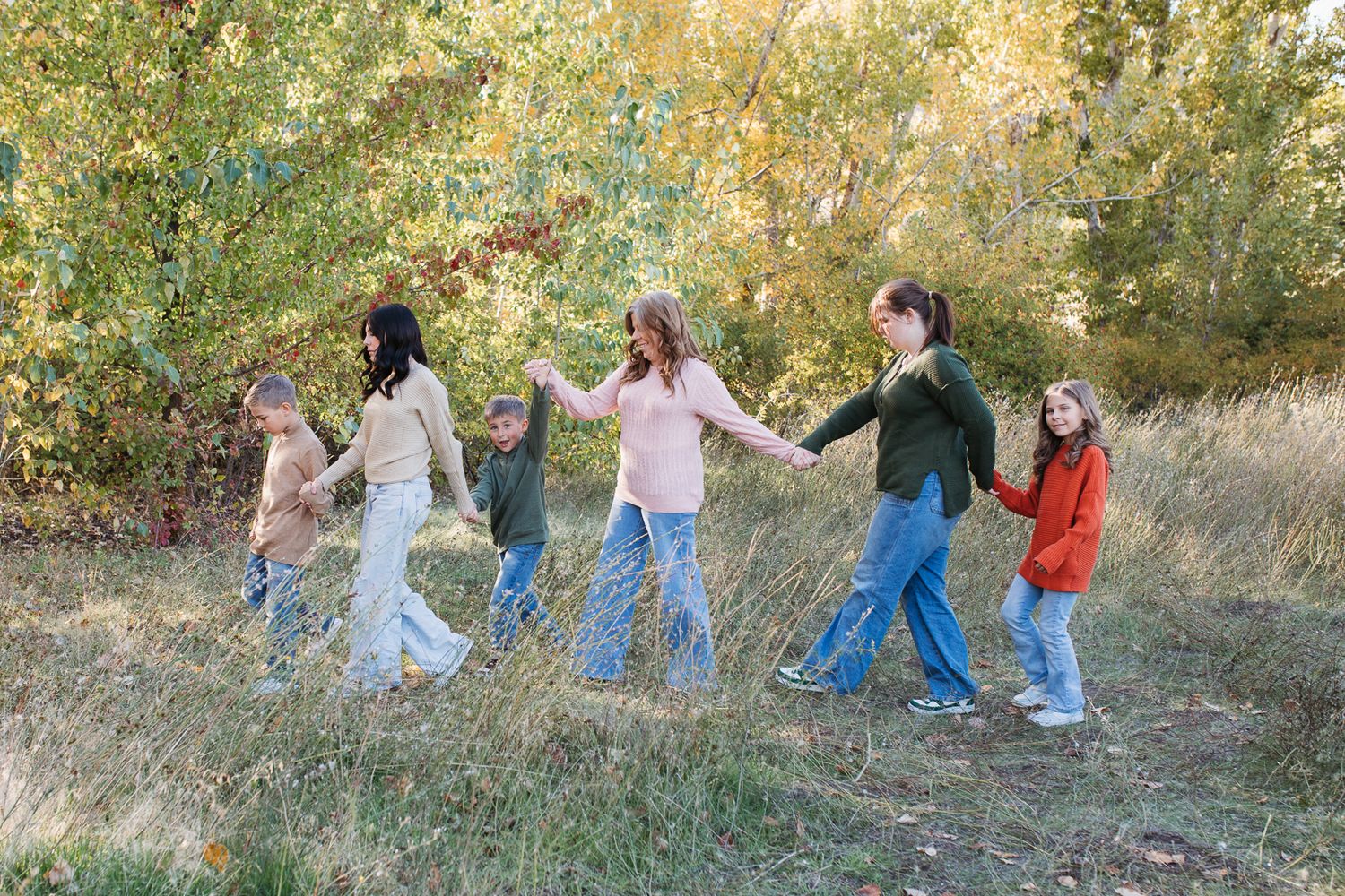 A family walking holding hands in a grassy outdoor setting during autumn. Boise foothills family photography