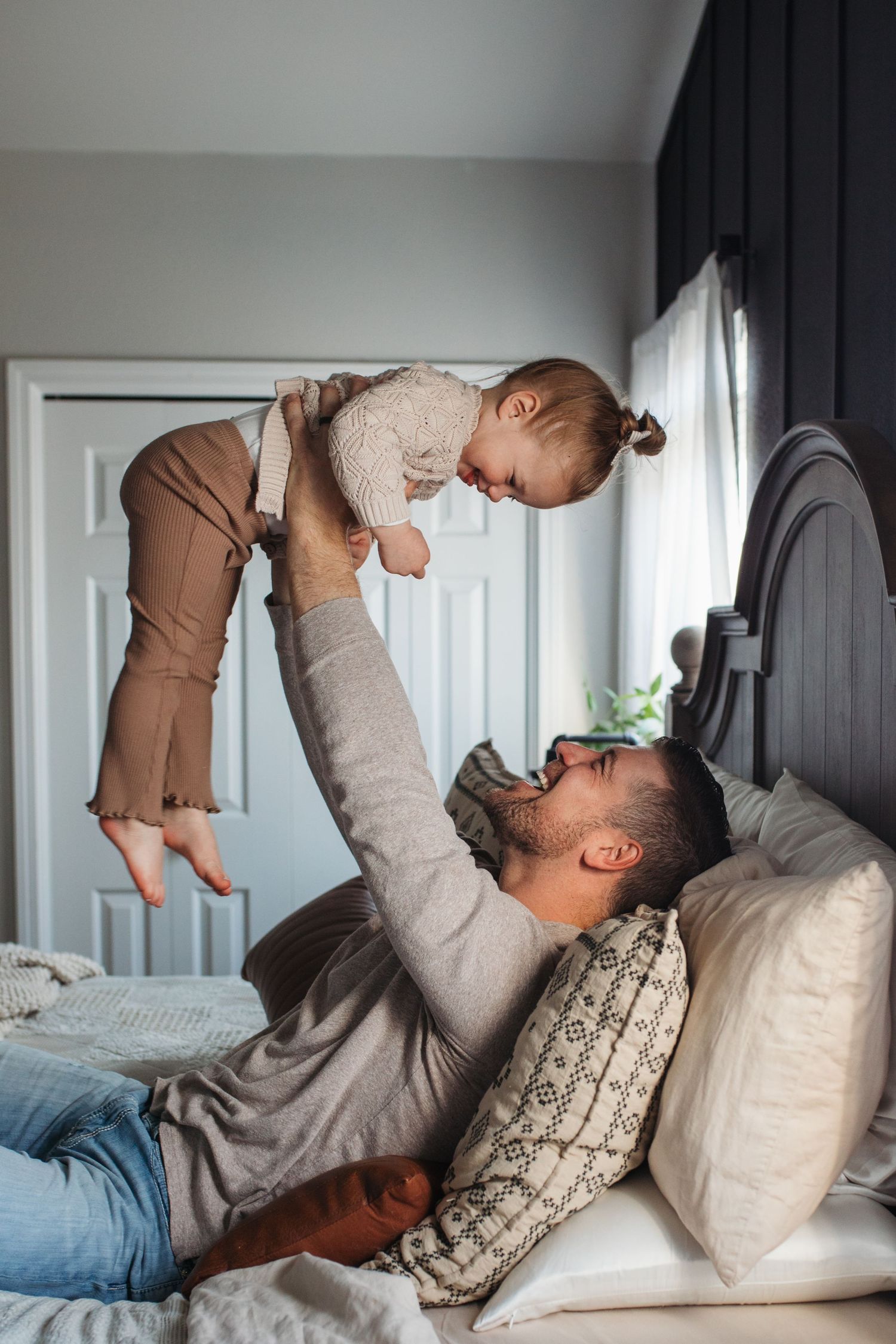 A parent lying on a bed lifts and plays with a baby wearing brown clothing in a series of four photos in-home lifestyle family photos Boise