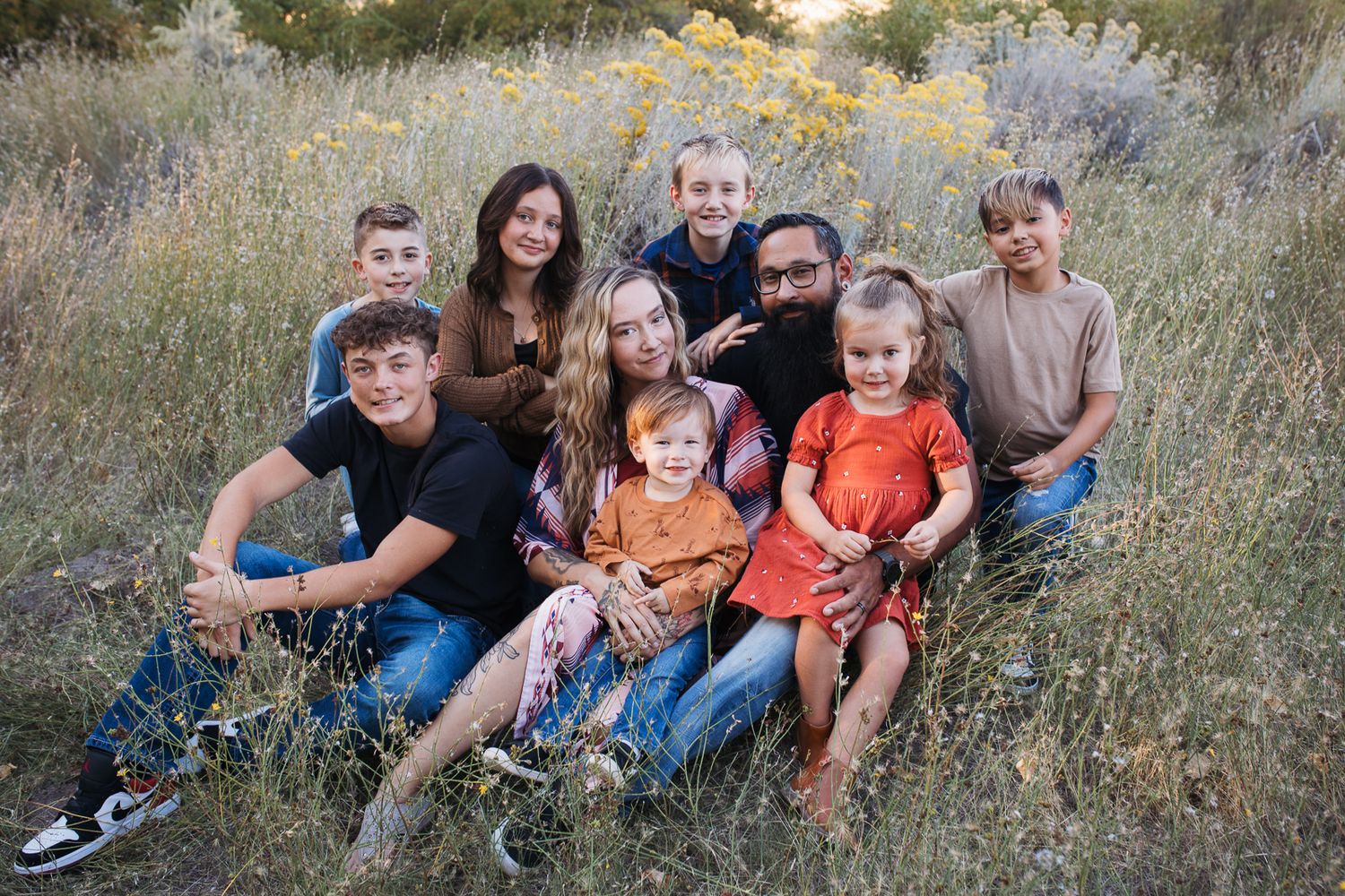 A large family sits together in a grassy field during golden hour for a casual outdoor photo session - lifestyle family photos Boise