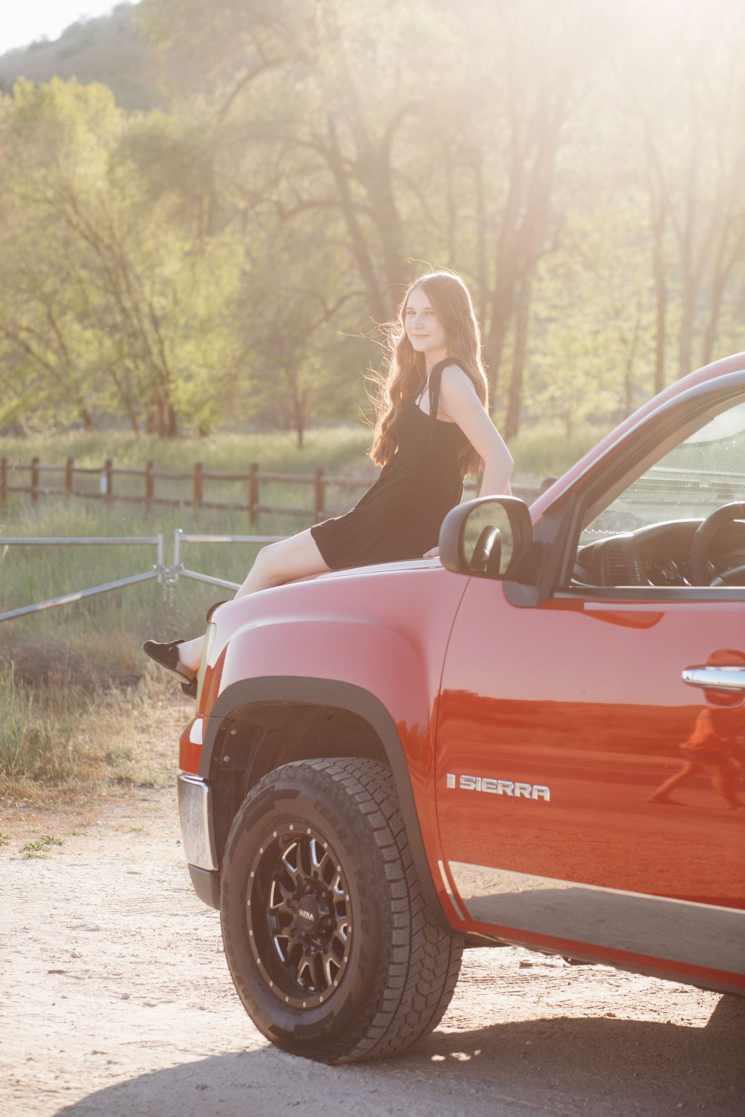 Boise senior photos of high school girl sitting on red truck hood in golden hour light during outdoor senior session