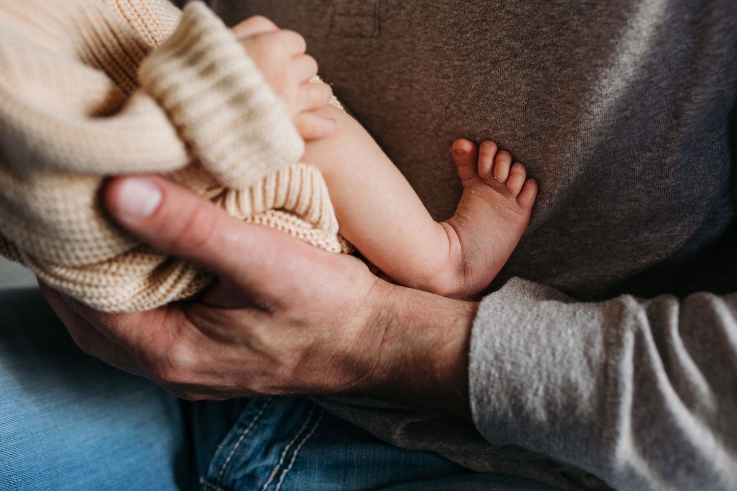 Close-up shots of gentle hands holding and comforting a baby in soft knit clothing - lifestyle in-home newborn photos Boise