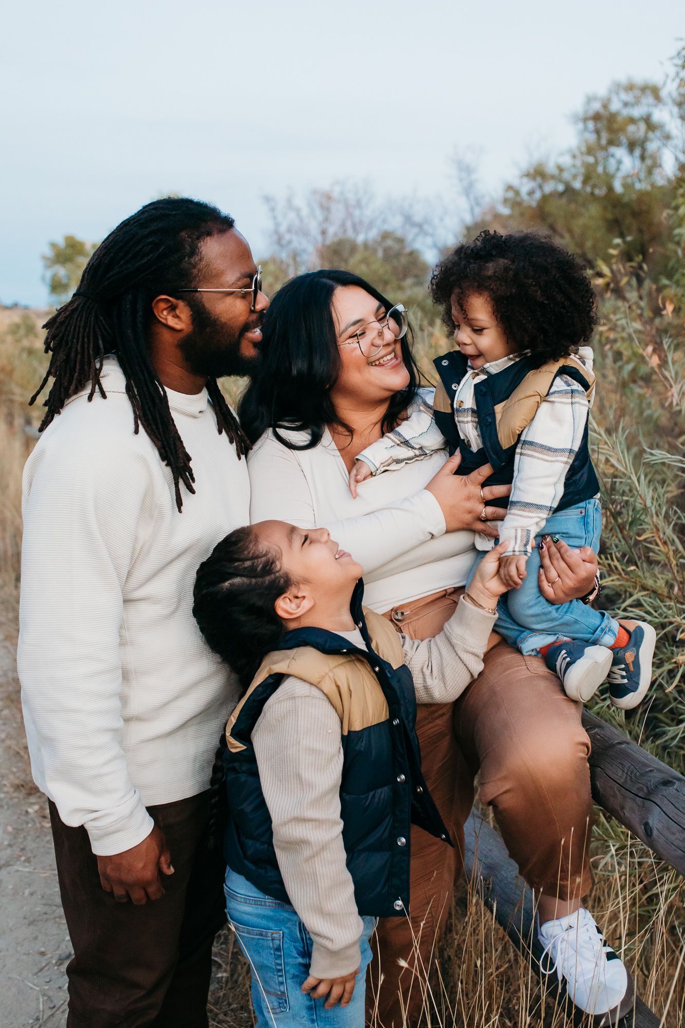 A joyful family shares laughter and embraces while posing together outdoors in matching cream-colored outfits - lifestyle family photos