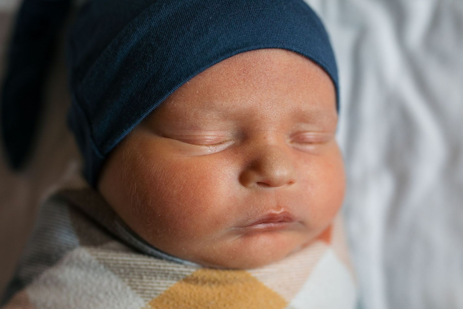 Fresh 48 session by Sara Elizabeth Photography, a Close-up view shows a tranquil newborn baby sleeping peacefully swaddled in soft blankets.