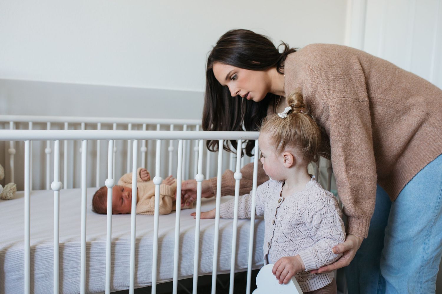 Mother helping her toddler meet the new baby in the crib during an in-home lifestyle newborn session in Boise, Idaho.