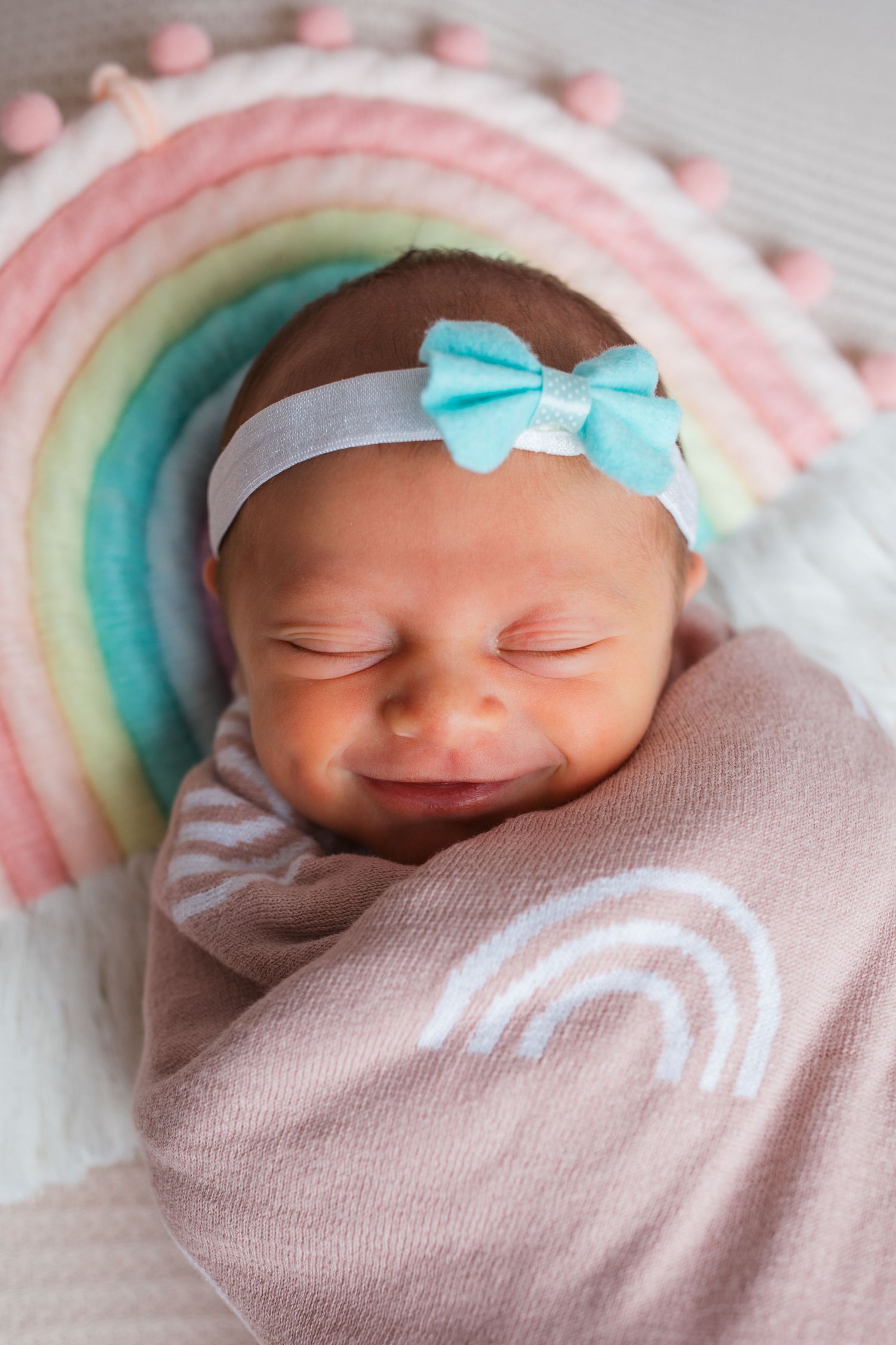 Smiling newborn baby girl wrapped in pink and posed with a pastel rainbow during a newborn photography session in Nampa, Idaho.