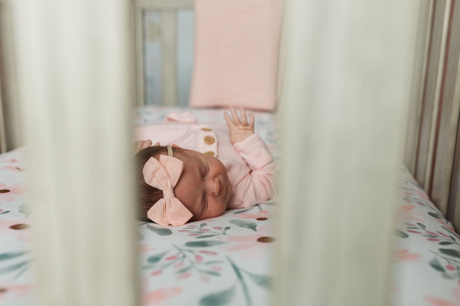 Newborn baby girl sleeping in her floral crib in Middleton, Idaho, photographed through the crib slats during a lifestyle session.