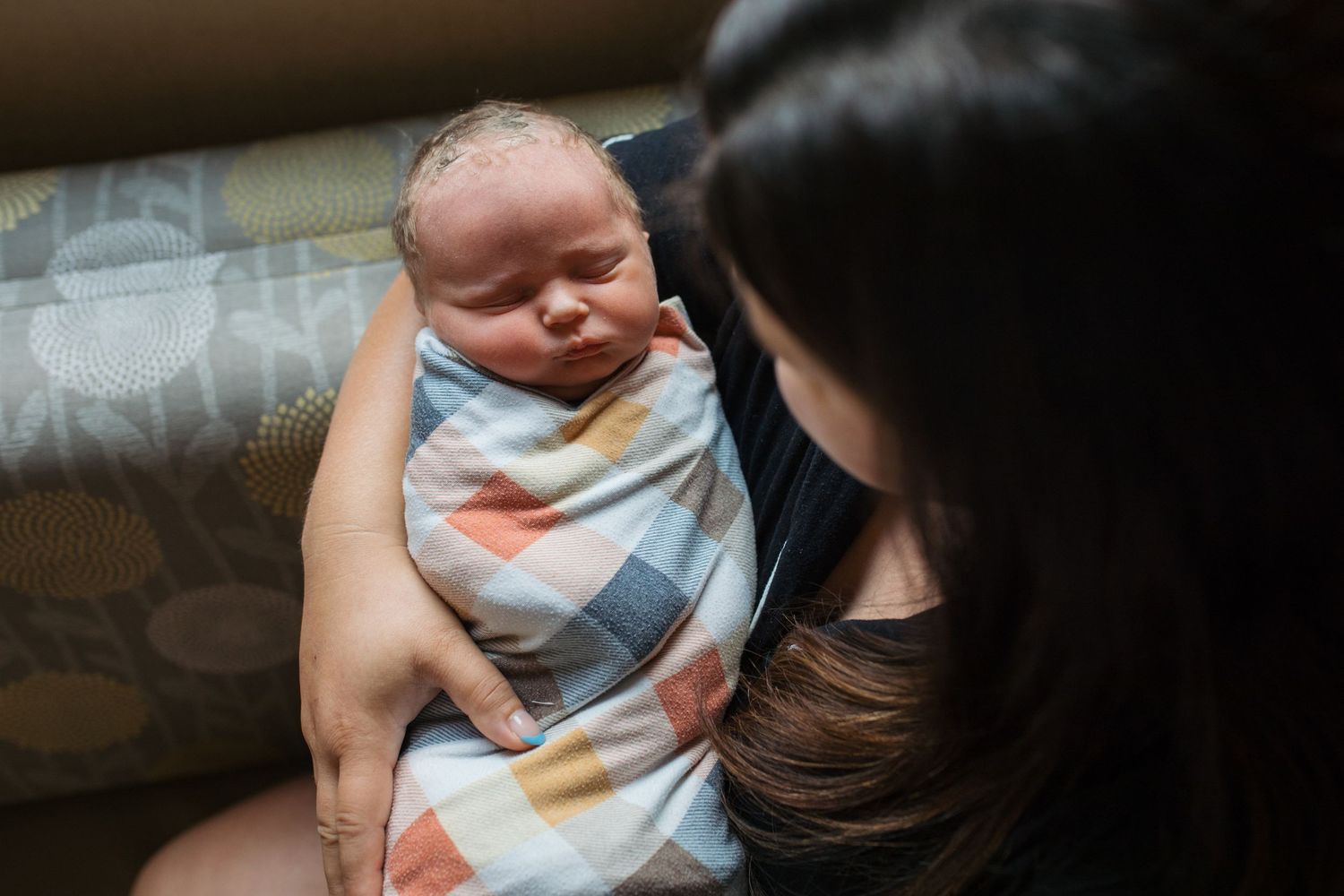 Parent holds sleeping infant wrapped in blue and white blanket while sitting on couch - Fresh 48 session in Boise, Idaho