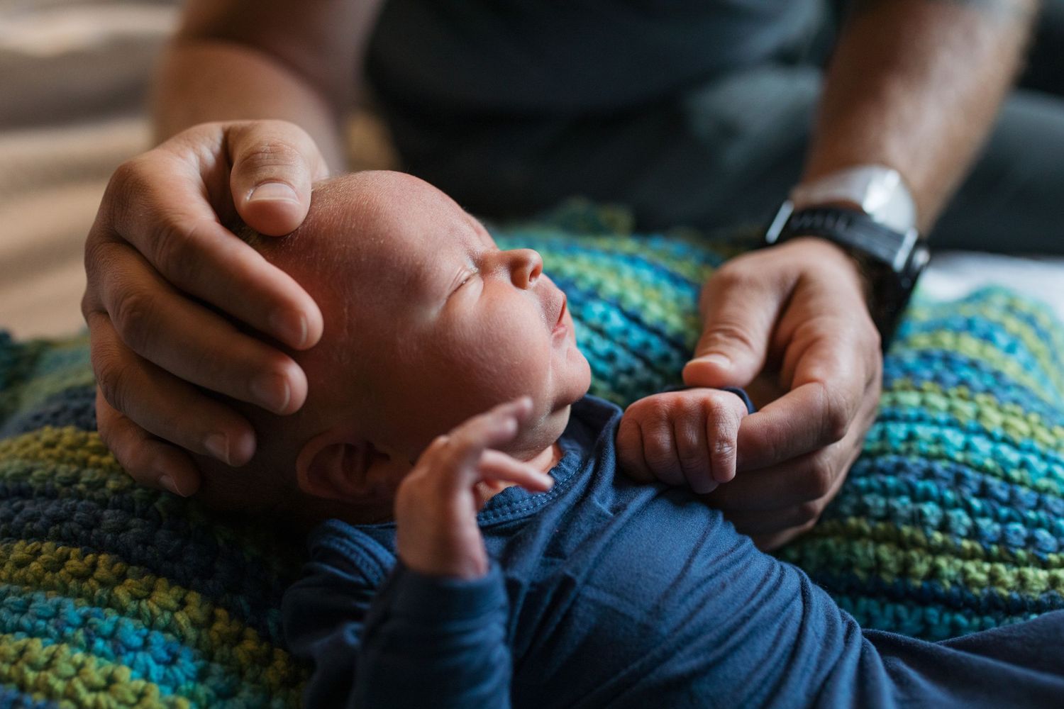 A newborn baby lies on a striped blanket while being gently held by caring hands - Fresh 48 session in hospital Boise, Idaho