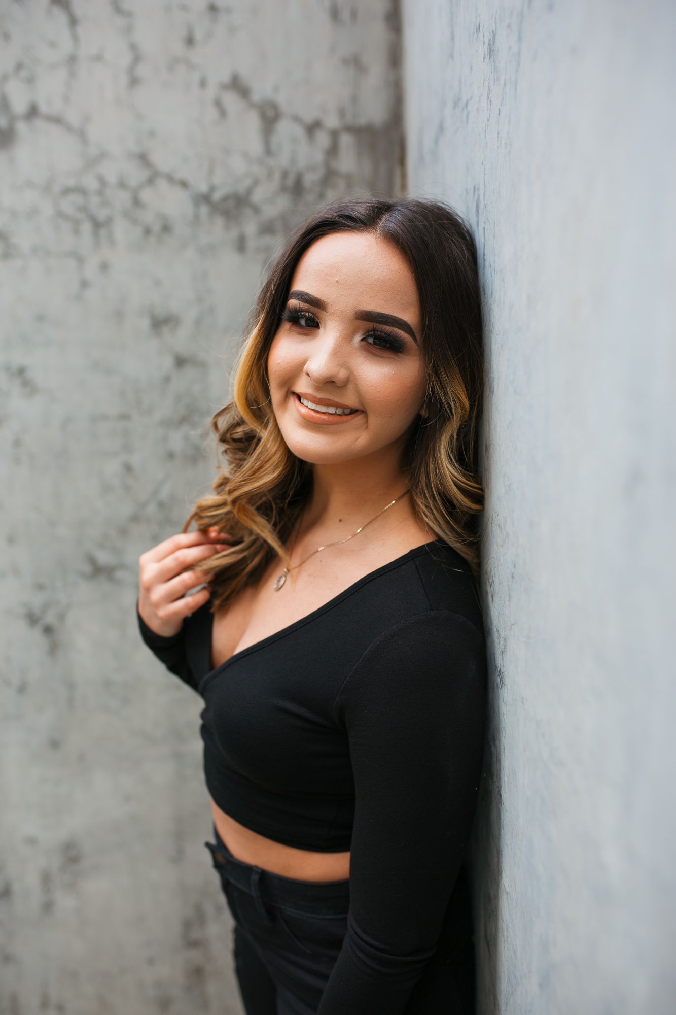 A woman in a black crop top poses against a concrete wall in a series of four stylish portrait photos - Senior photos Boise Idaho