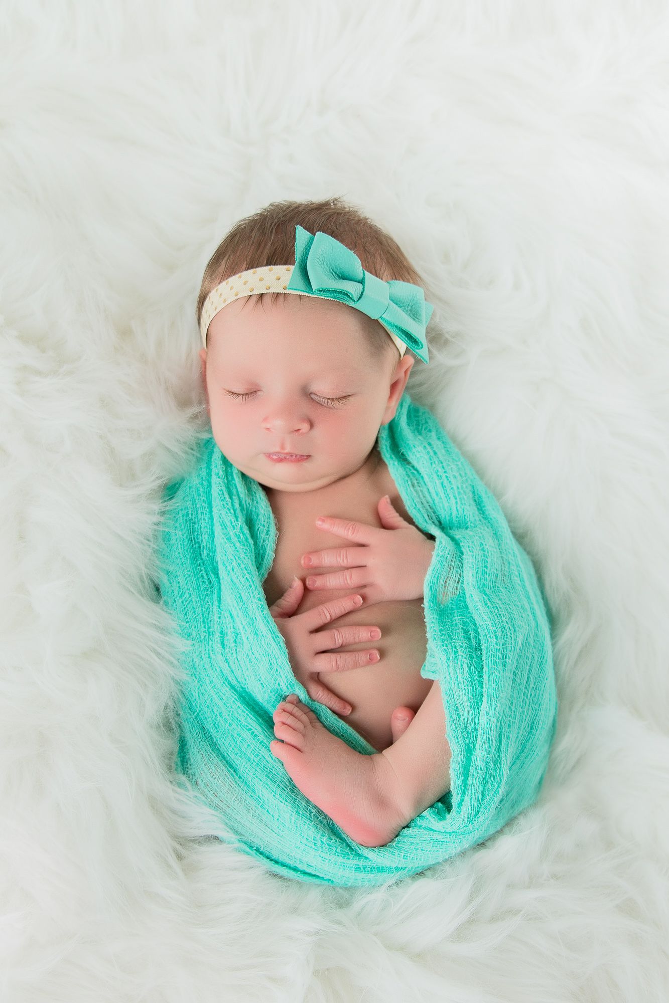 Sleeping newborn wrapped in soft turquoise fabric with matching bow headband on white fluffy background -studio newborn photography Idaho