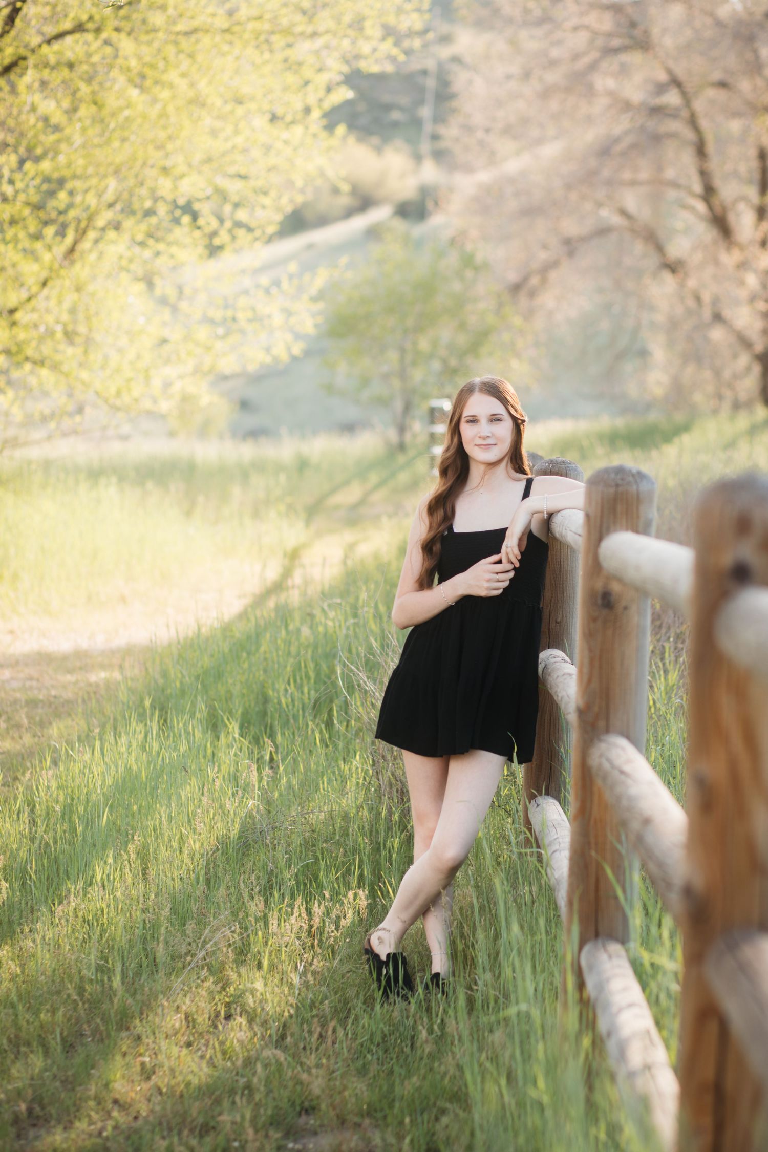 Boise senior portrait of high school girl standing by wooden fence in black dress during outdoor golden hour session