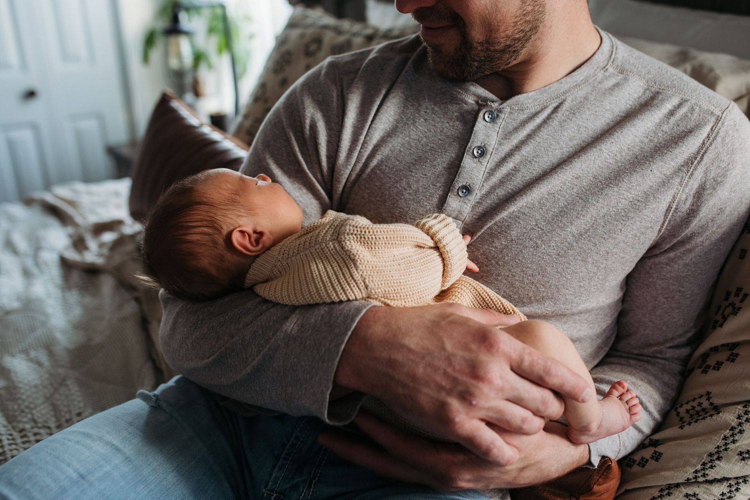 A parent holds a sleeping newborn baby while resting on a bed at home - lifestyle in-home newborn photos Boise