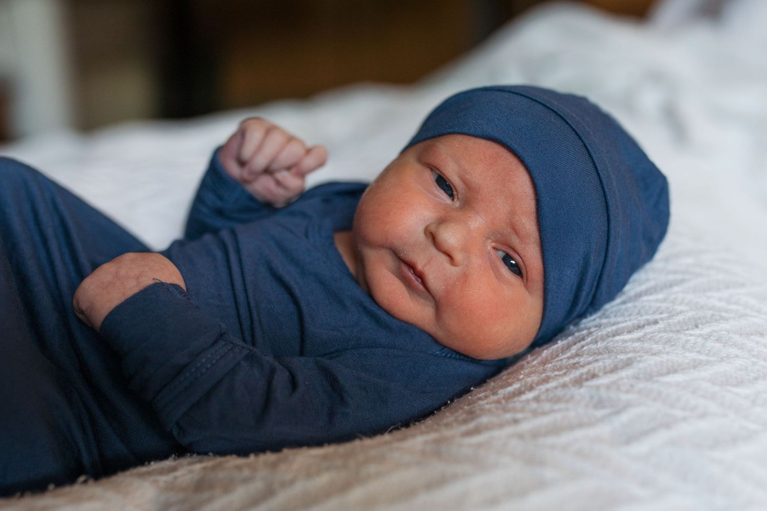 newborn baby wearing a navy blue outfit lying on white bedding in hospital. Fresh 48 session by Sara Elizabeth Photography Boise Idaho