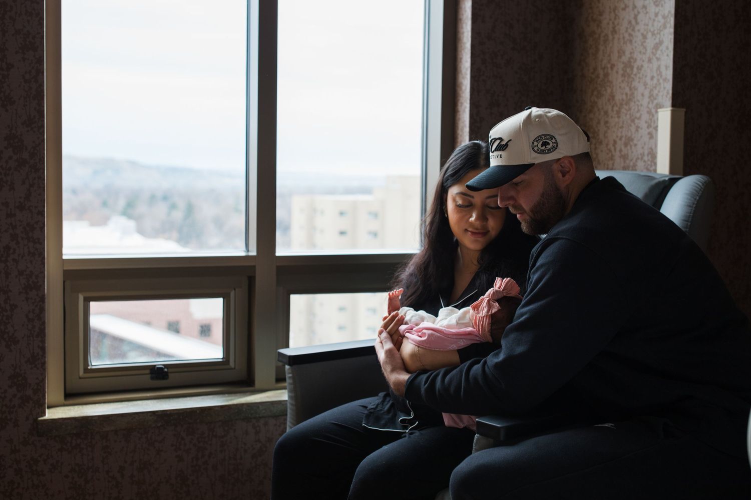 Parents holding their newborn by the hospital window during a Fresh 48 photography session in Boise