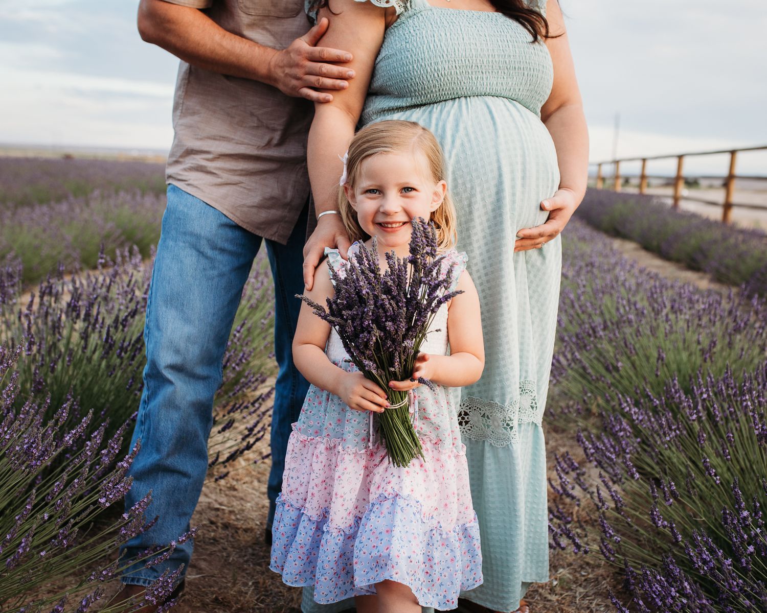 Family wearing coordinating outfits poses together in a blooming purple lavender field at sunset - Maternity session in Boise, Idaho