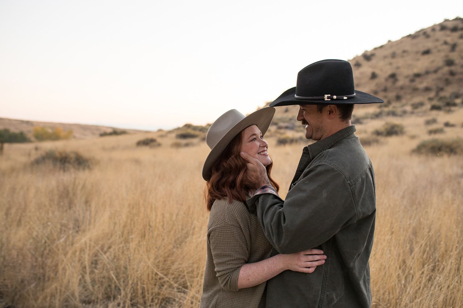 A couple embraces lovingly in a golden field of tall grass during sunset in a desert landscape- lifestyle family photos in Boise