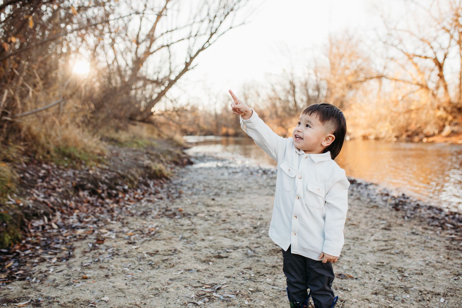 A series of outdoor family photos taken at sunset along a riverbank with golden autumn light filtering through trees - lifestyle family