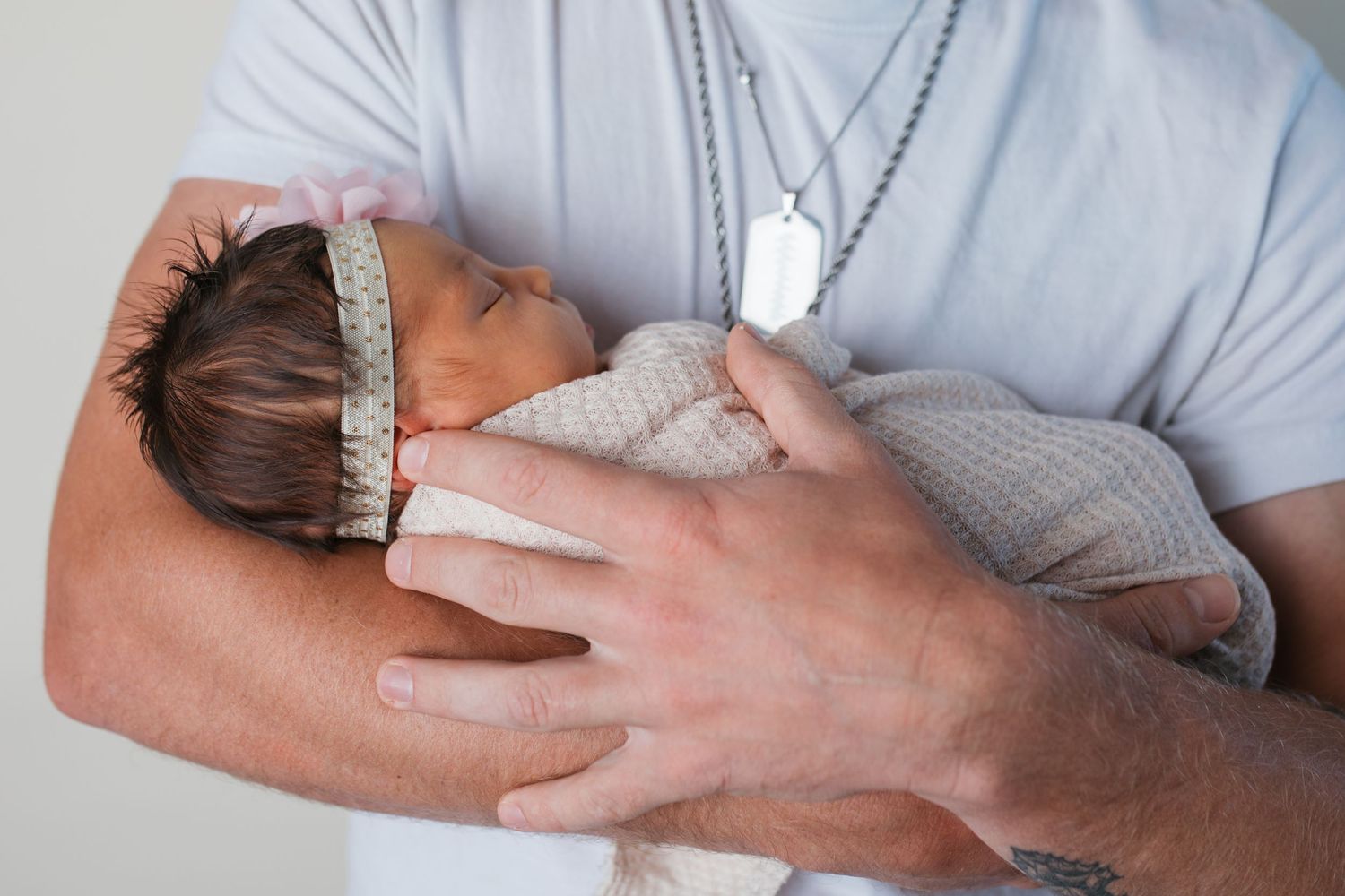 Dad holding sleeping newborn baby girl wrapped in neutral blanket during Caldwell, Idaho newborn photography session