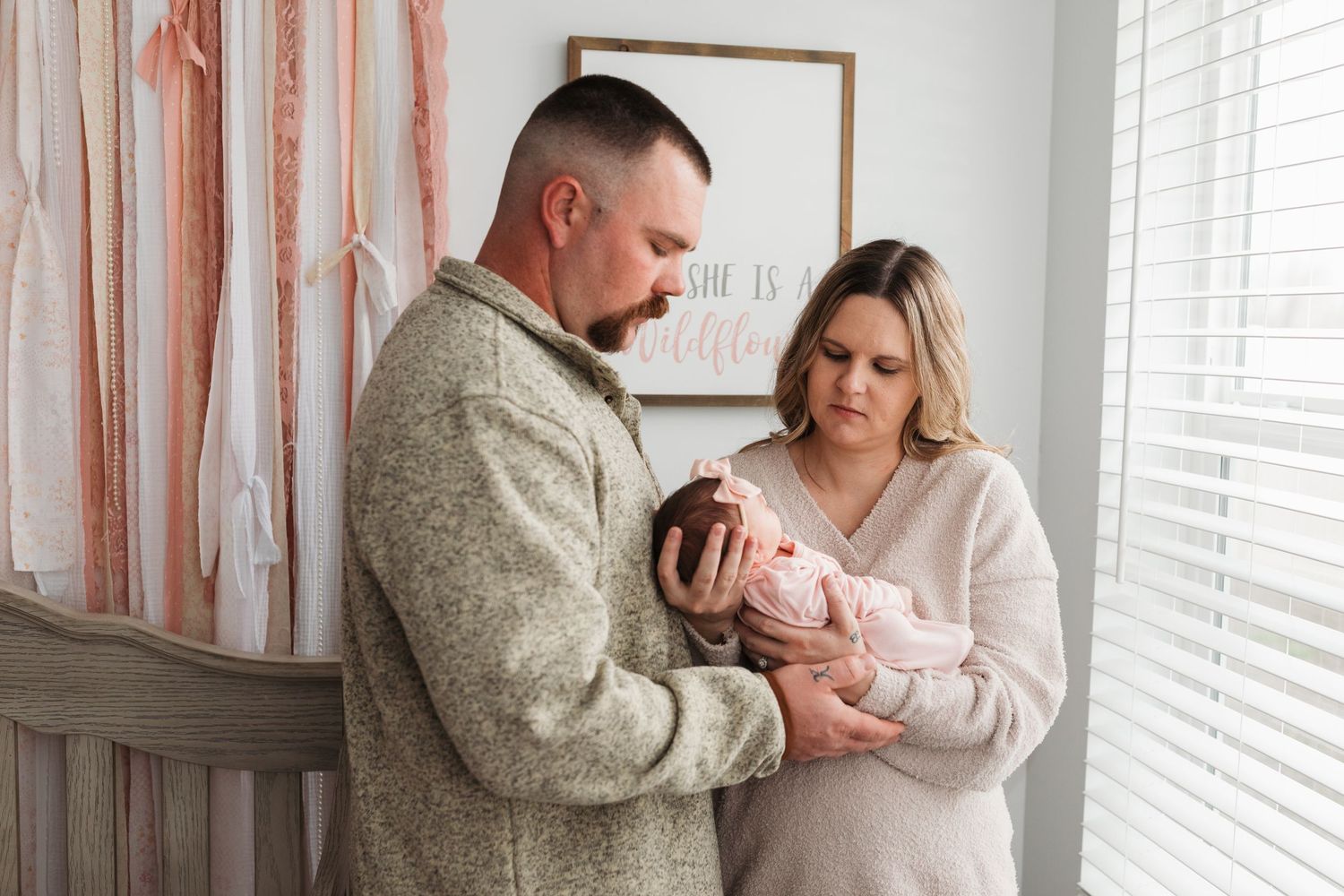 In-home lifestyle newborn session in Boise with parents holding their baby girl in her nursery by window light