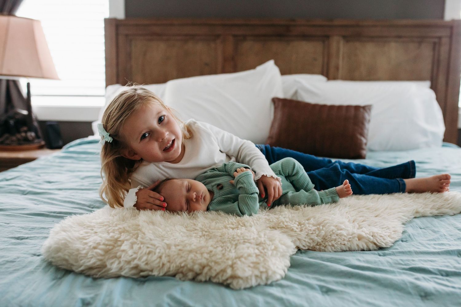 Older sister cuddling newborn baby on bed during in-home lifestyle newborn session in Boise, Idaho