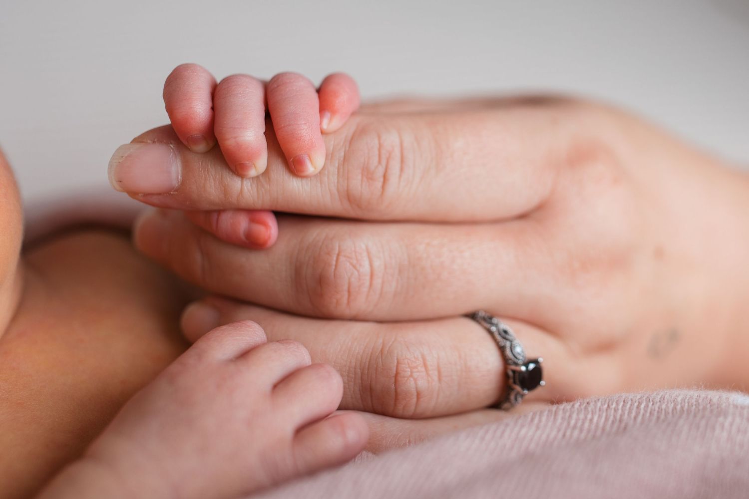 Close up of a newborn baby’s tiny hand resting against her parent’s hand during a newborn photography session.