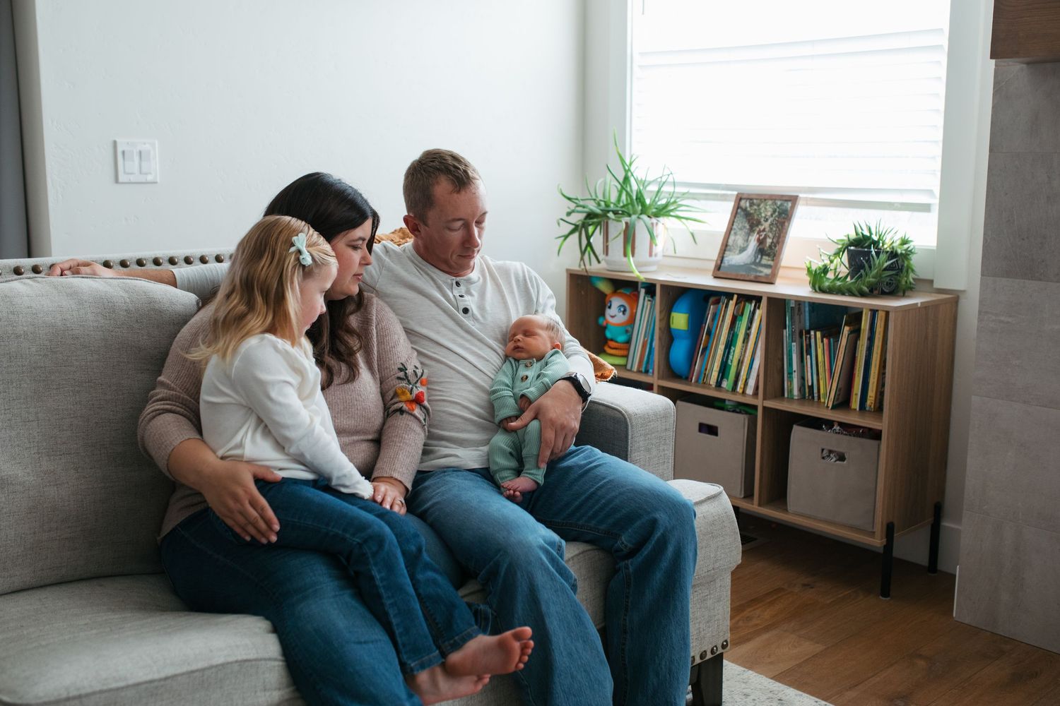 Boise lifestyle newborn session with parents and sibling cuddling their newborn baby on the couch in soft natural light