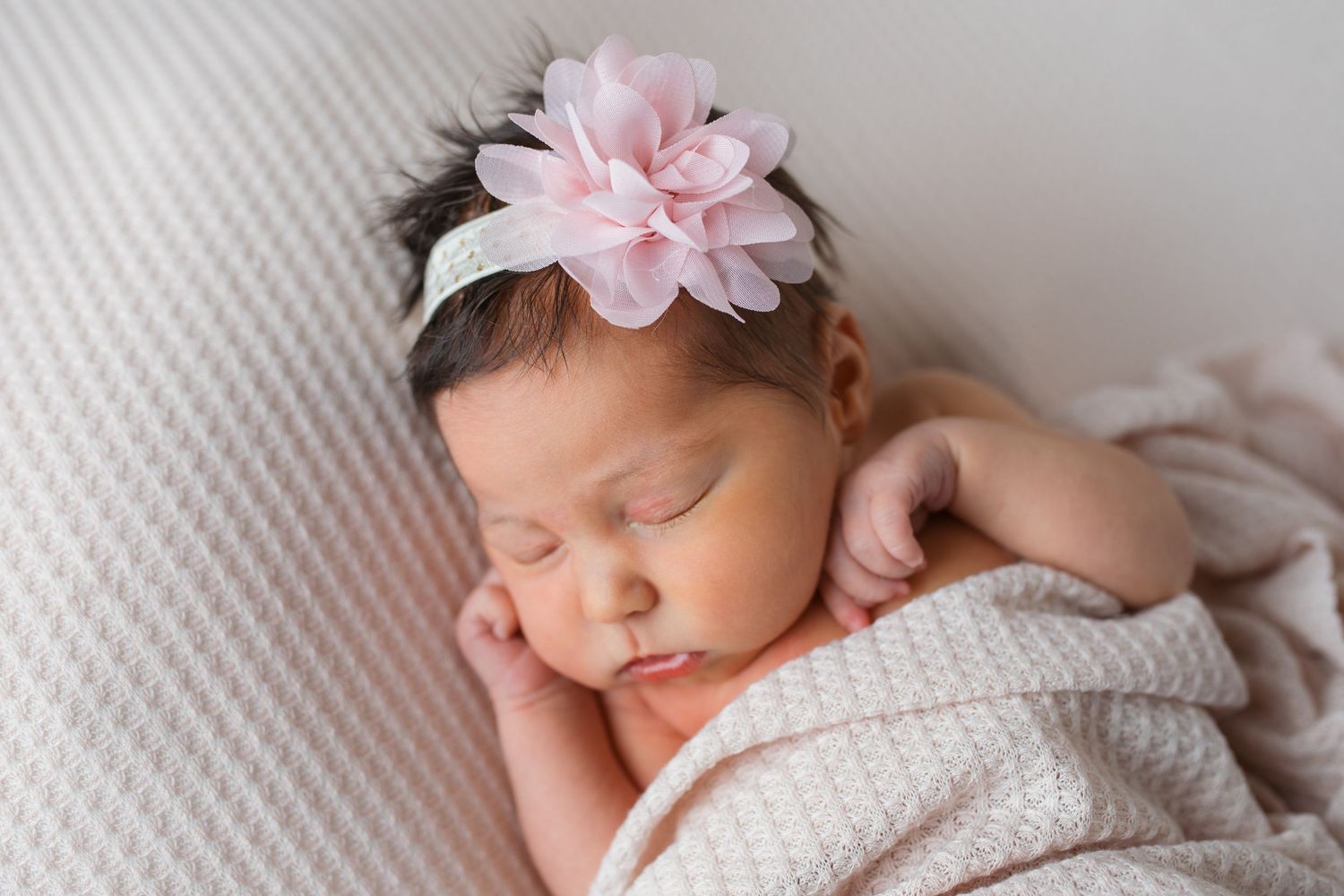 Studio newborn portrait in Caldwell, Idaho of sleeping baby girl wrapped in neutral blanket with pink floral headband