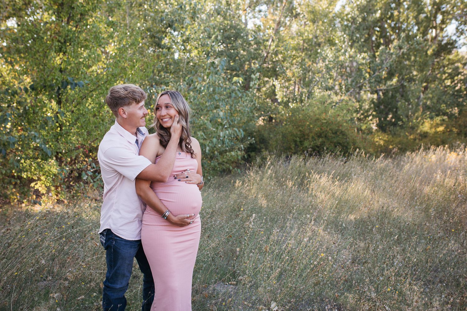 A couple expecting embraces in a golden sunlit field during a romantic outdoor photo session - Maternity session in Boise
